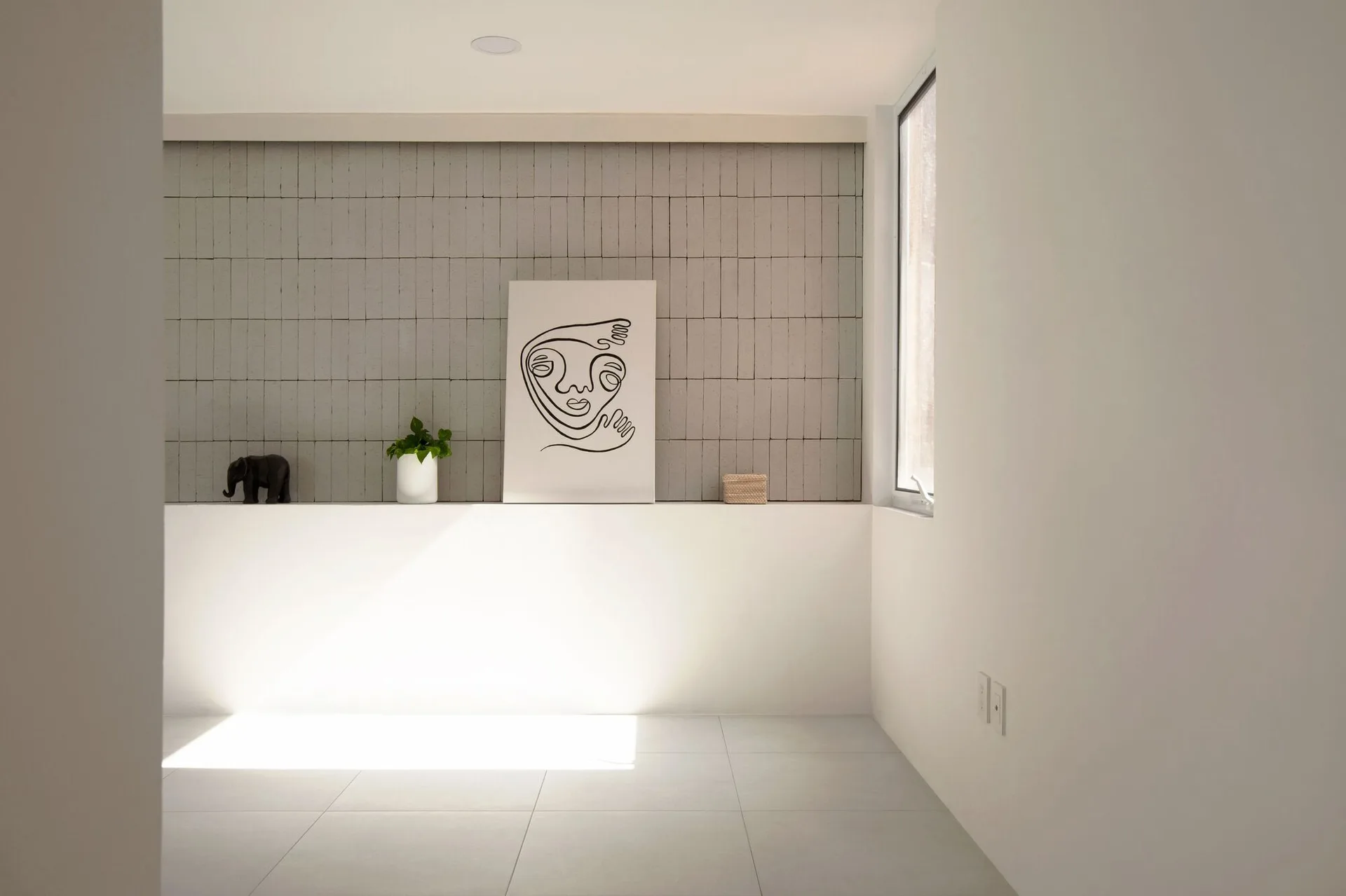 A minimalist white display ledge with modern line art and small decor items set against a vertically stacked grey tile feature wall.
