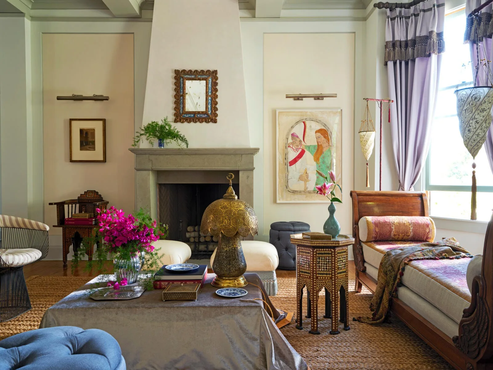 An eclectic living room featuring a stone fireplace, a wooden chaise longue, and lavender curtains over a textured woven rug.