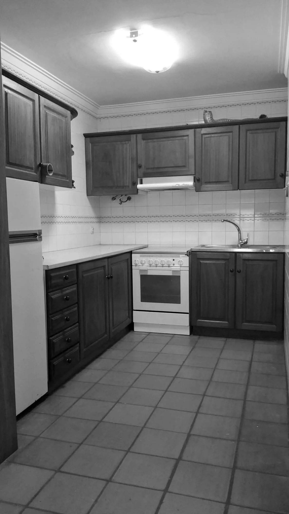A traditional kitchen featuring dark wood cabinetry, white appliances, and square floor and wall tiles.