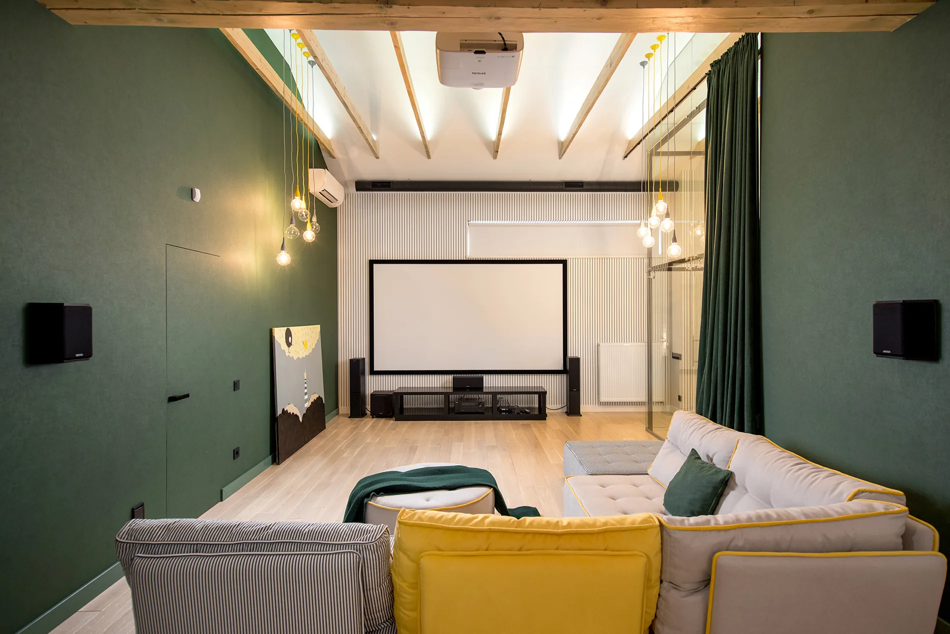 A modern home theater features dark green walls, a modular sectional sofa with yellow accents, and a large projection screen on a vertical slatted wall.