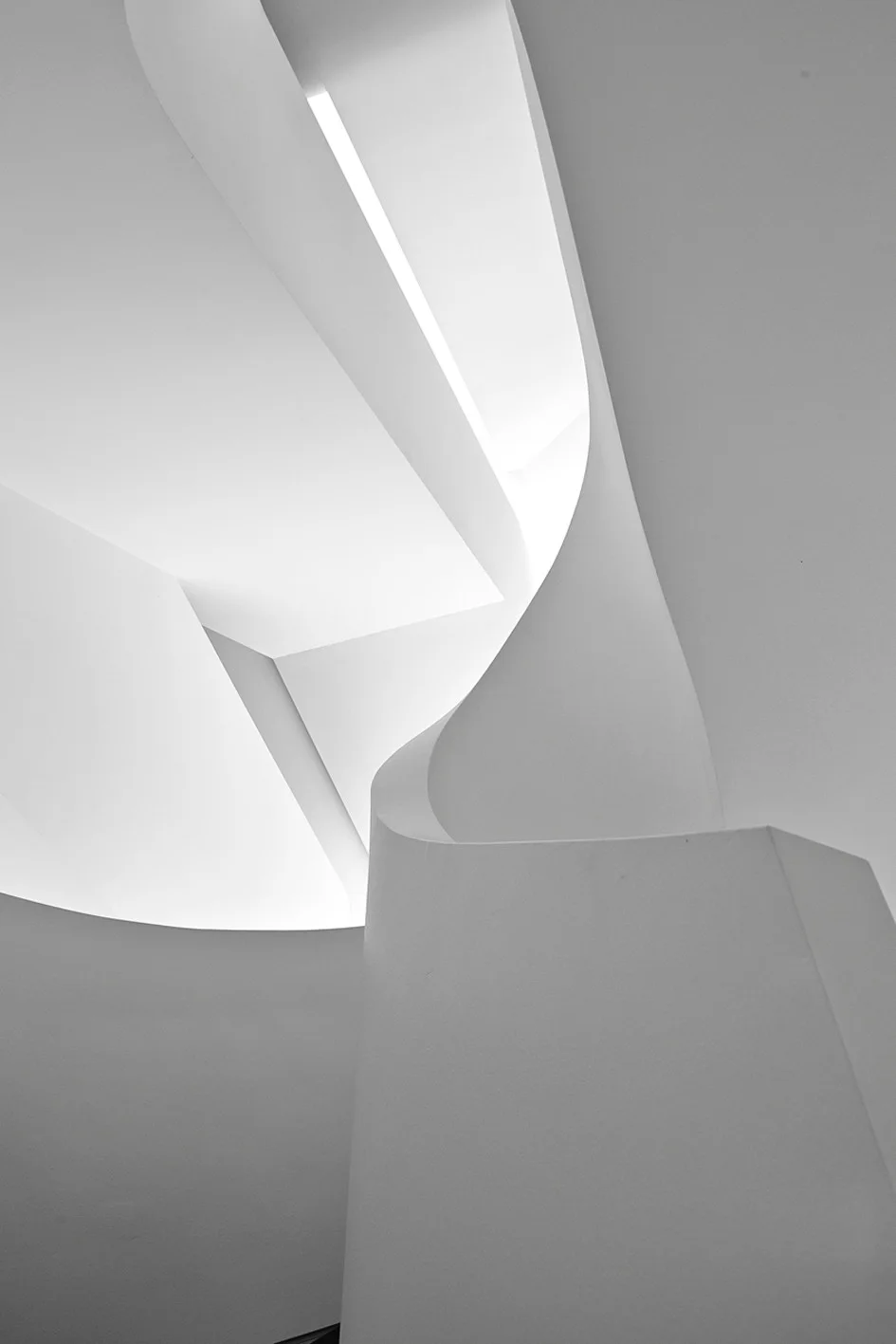 A close-up view of a minimalist white sculptural staircase showing smooth plaster-like curved walls and geometric architectural angles.