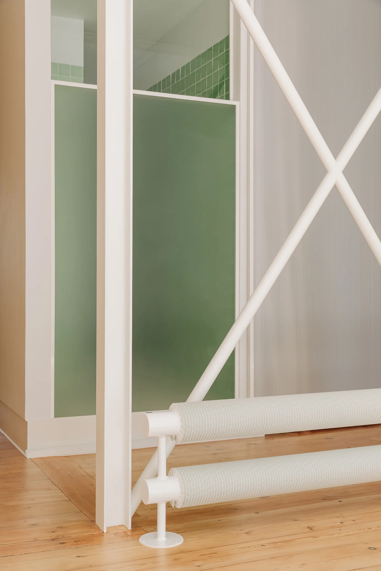 A modern room interior featuring a low white tubular radiator, light wood flooring, a white structural diagonal brace, and a green glass partition.