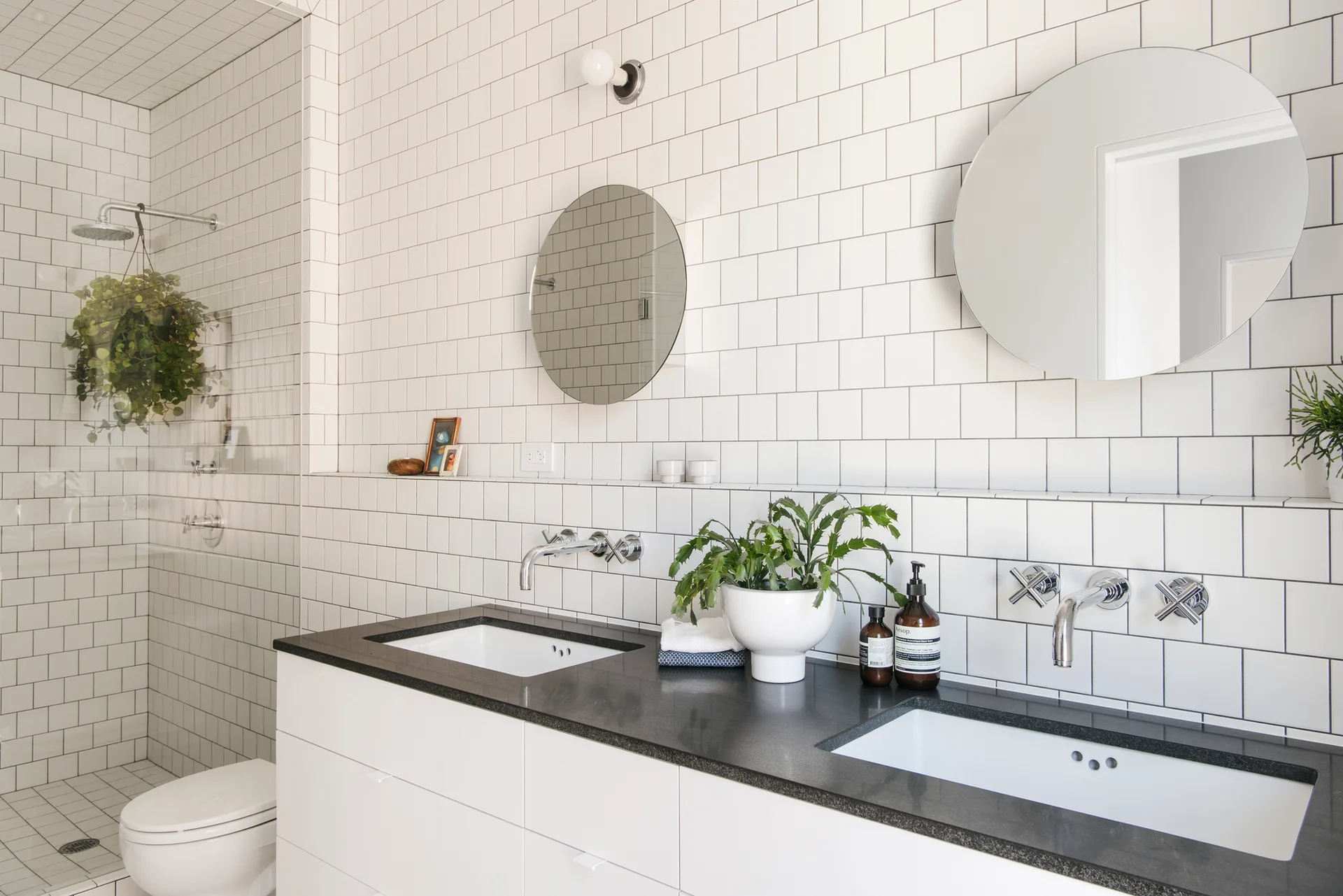 A modern bathroom with a double vanity, dark countertop, circular mirrors, and wall-mounted chrome faucets.