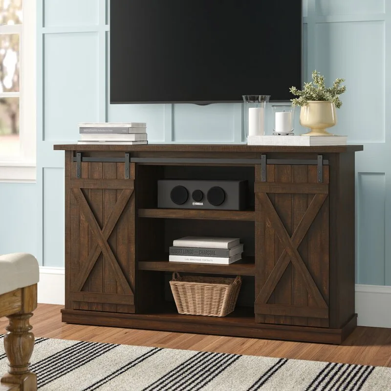 A dark brown wood media console with sliding barn doors stands against a light blue paneled wall beneath a wall-mounted television.