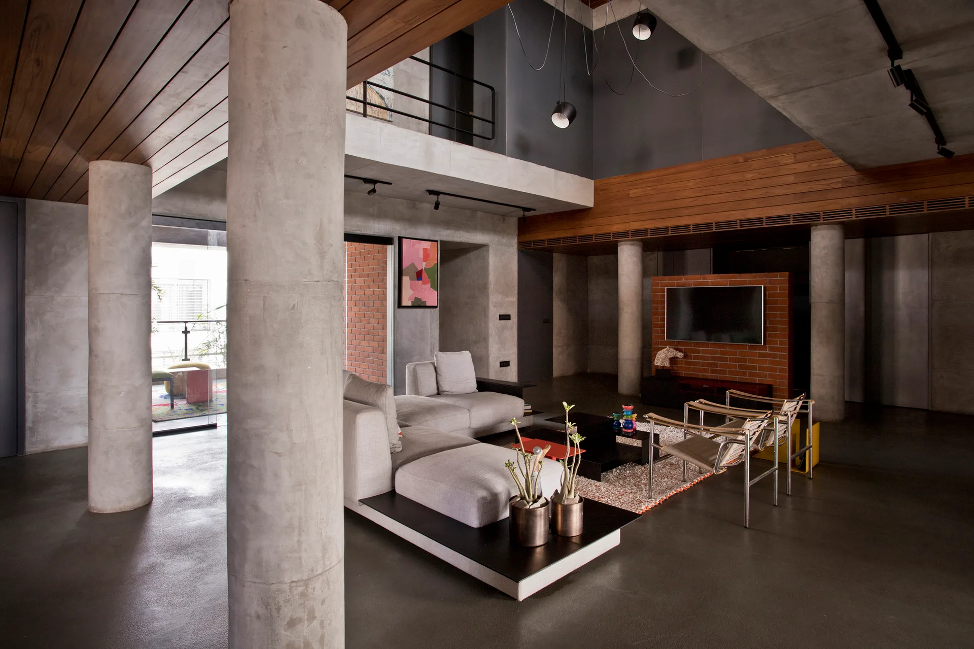 An industrial living room features prominent round concrete columns, a modular gray sofa, a brick partition wall, and wood ceiling slats.