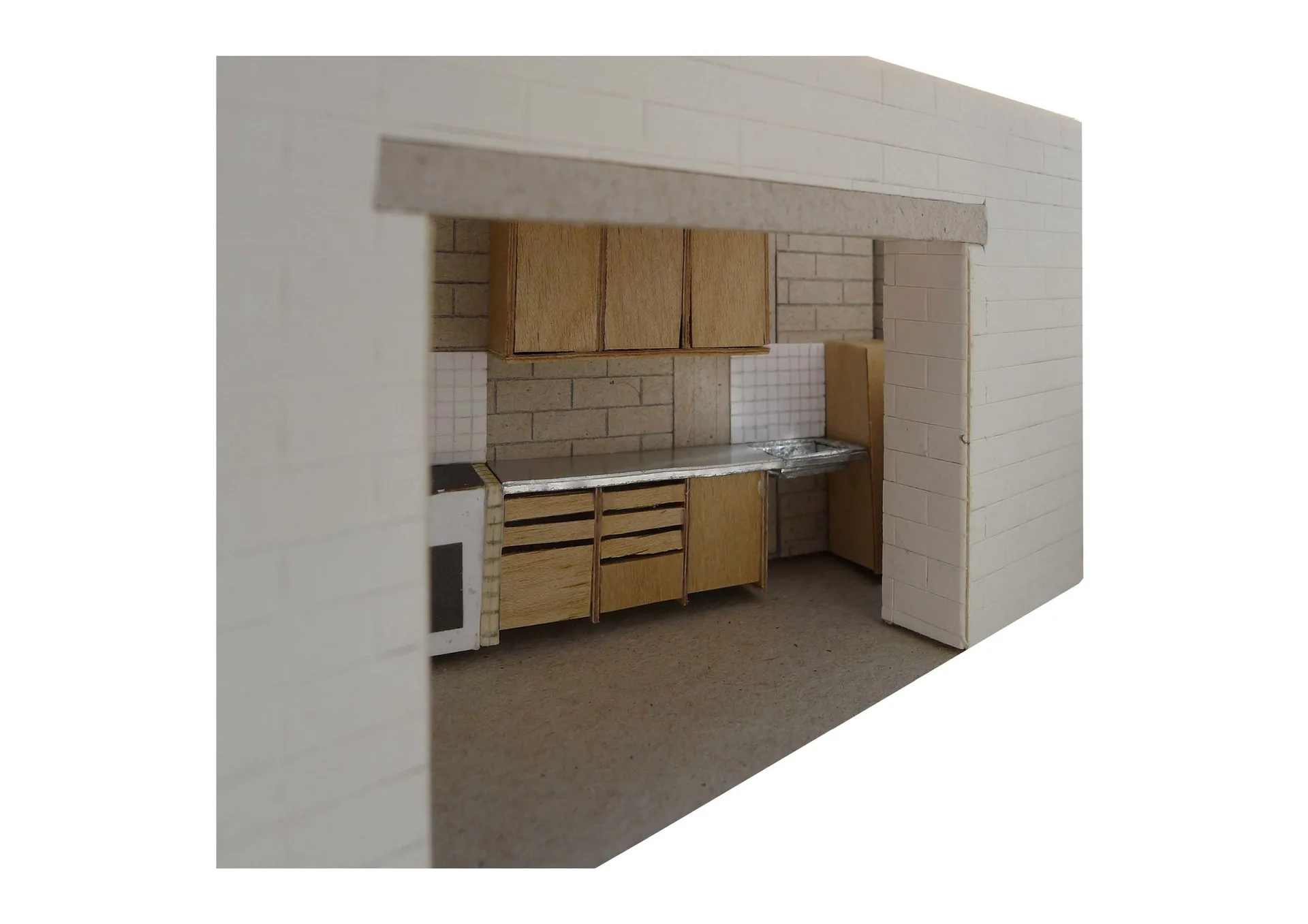 An architectural scale model displays a kitchen layout featuring light wood cabinets, a metallic countertop, and a tiled backsplash framed by a white archway.