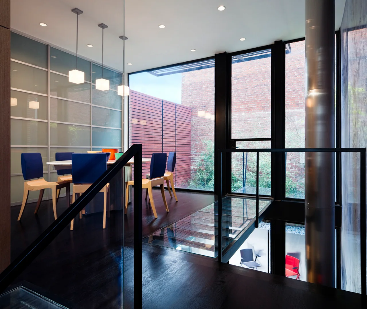 A modern dining room features a white oval table and blue chairs next to a glass floor walkway and floor-to-ceiling windows.