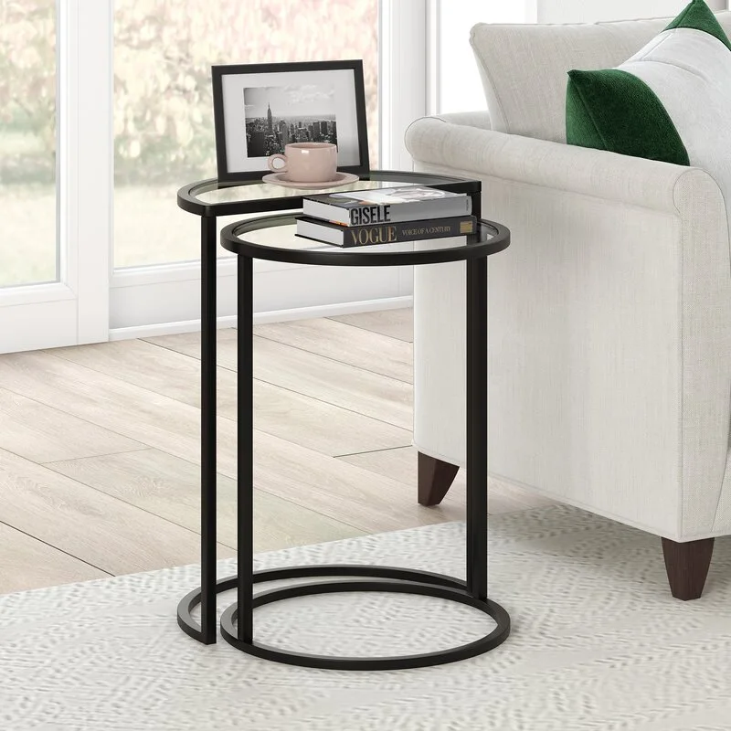 Two circular nesting side tables with black metal frames and glass tops sit on a textured white rug next to a light-colored sofa.