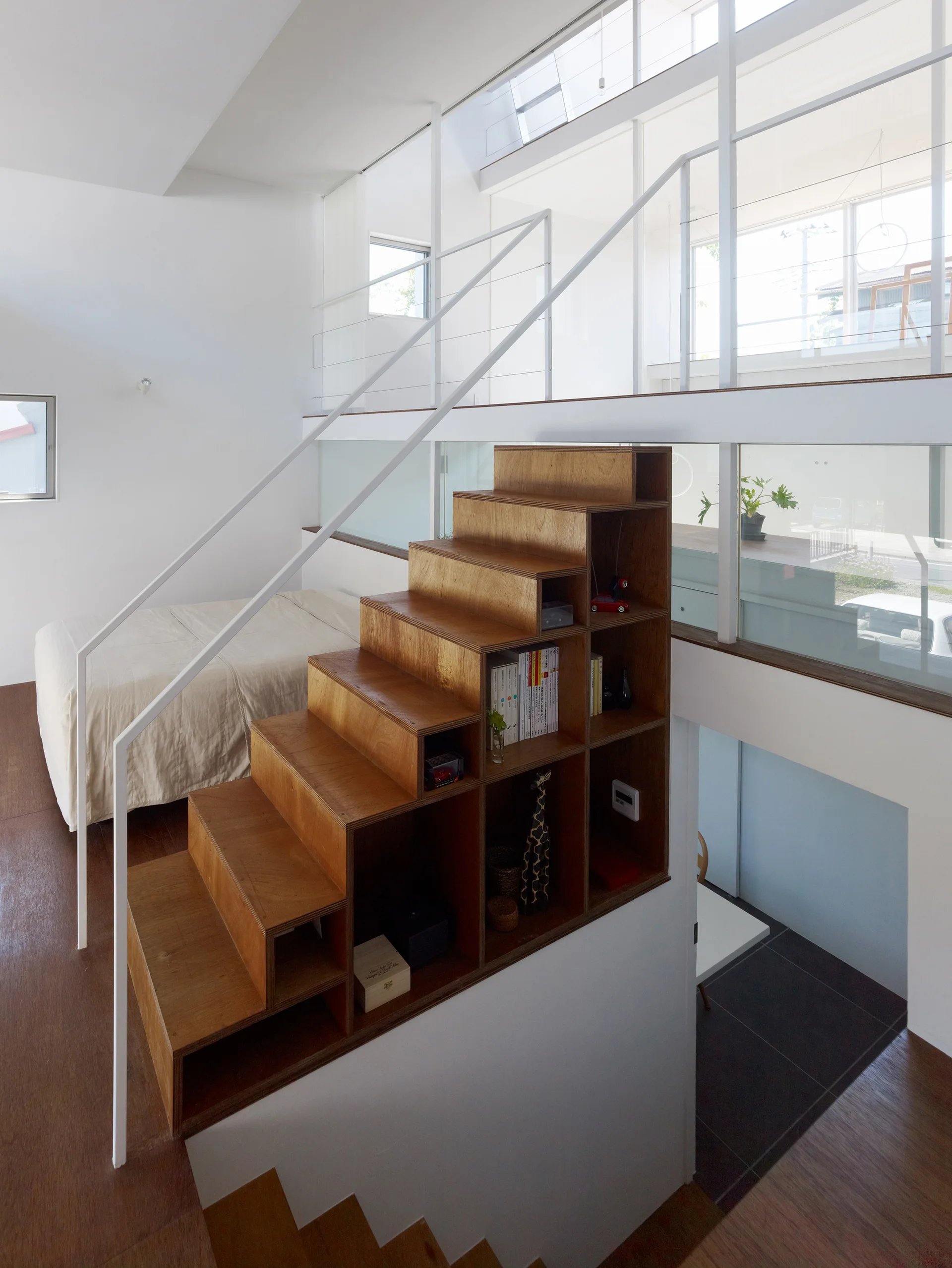 A modern plywood staircase features built-in storage cubbies filled with books and decor alongside white metal railings in a bright multi-level home.
