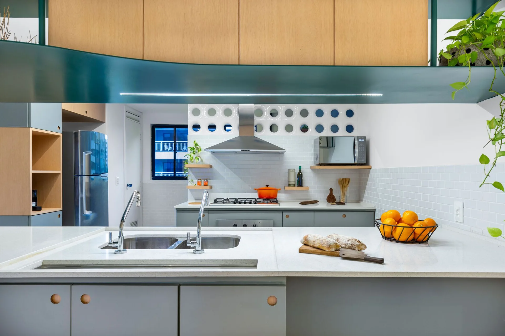 A modern kitchen features a gray kitchen island with a double sink, wood upper cabinets, and a white backsplash with circular cutouts.