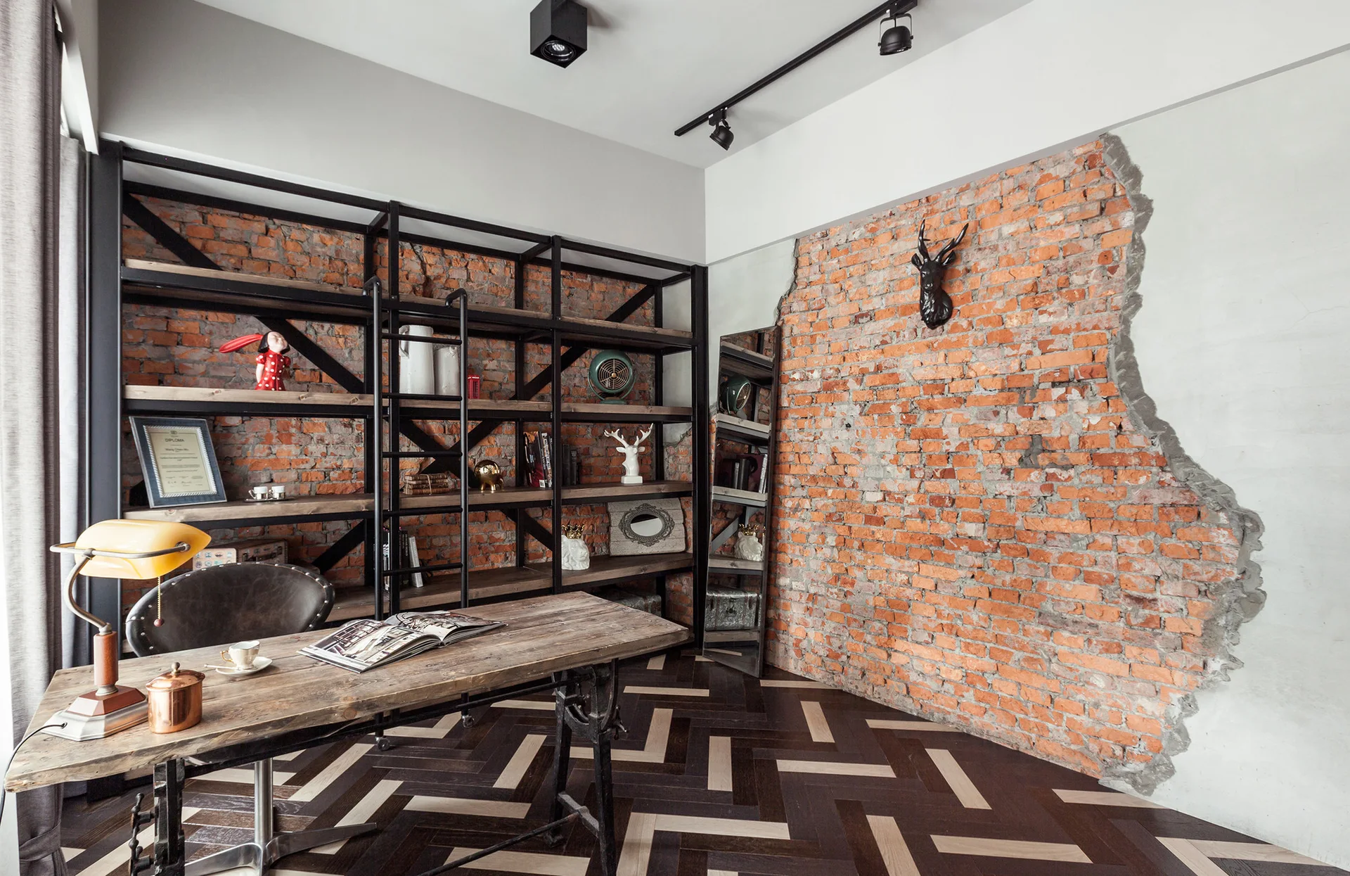 An industrial study features a reclaimed wood desk, a large black metal shelving unit, and a partially exposed brick wall.