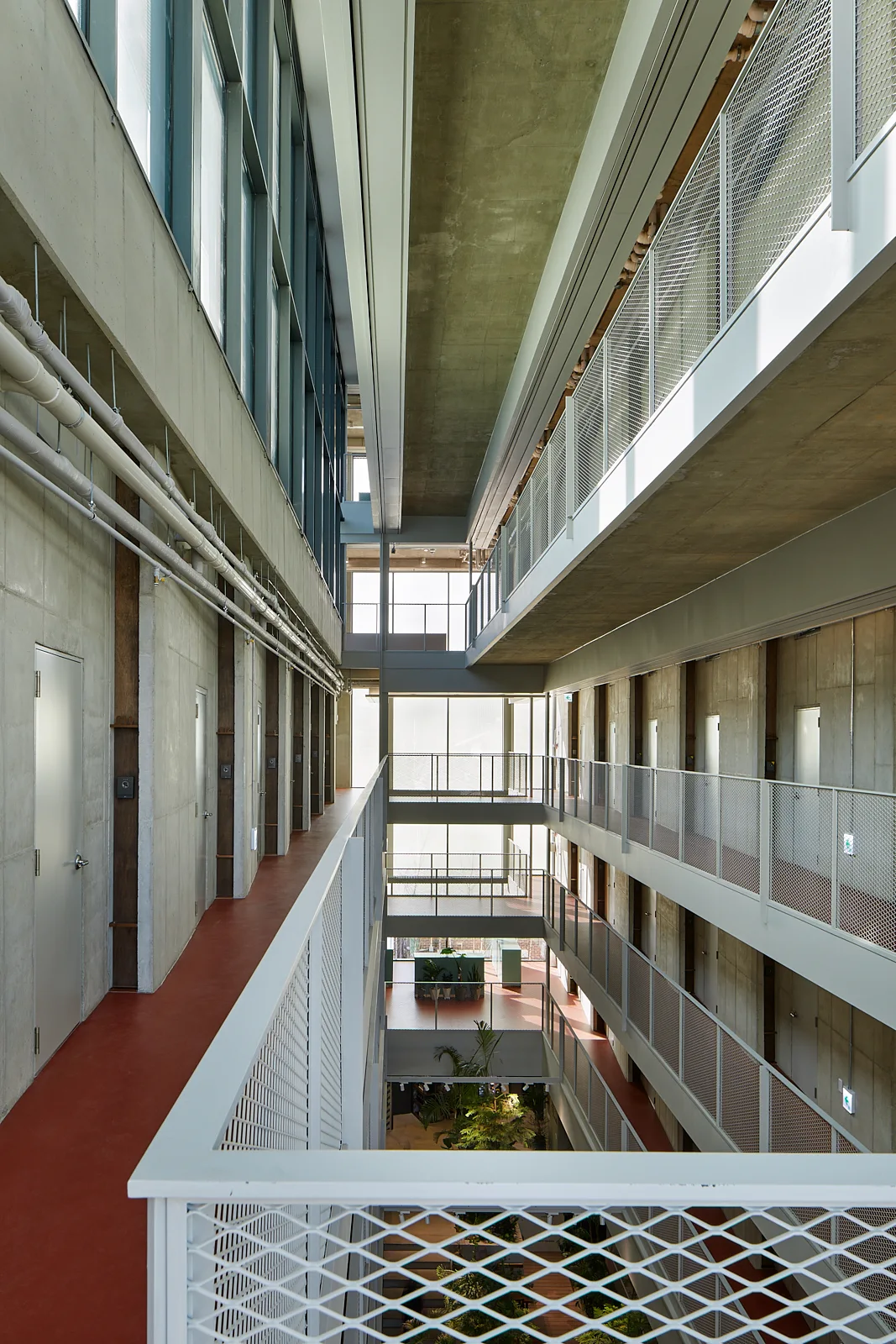 A multi-story industrial atrium featuring exposed concrete walls, terracotta-colored walkways, and white metal mesh railings.