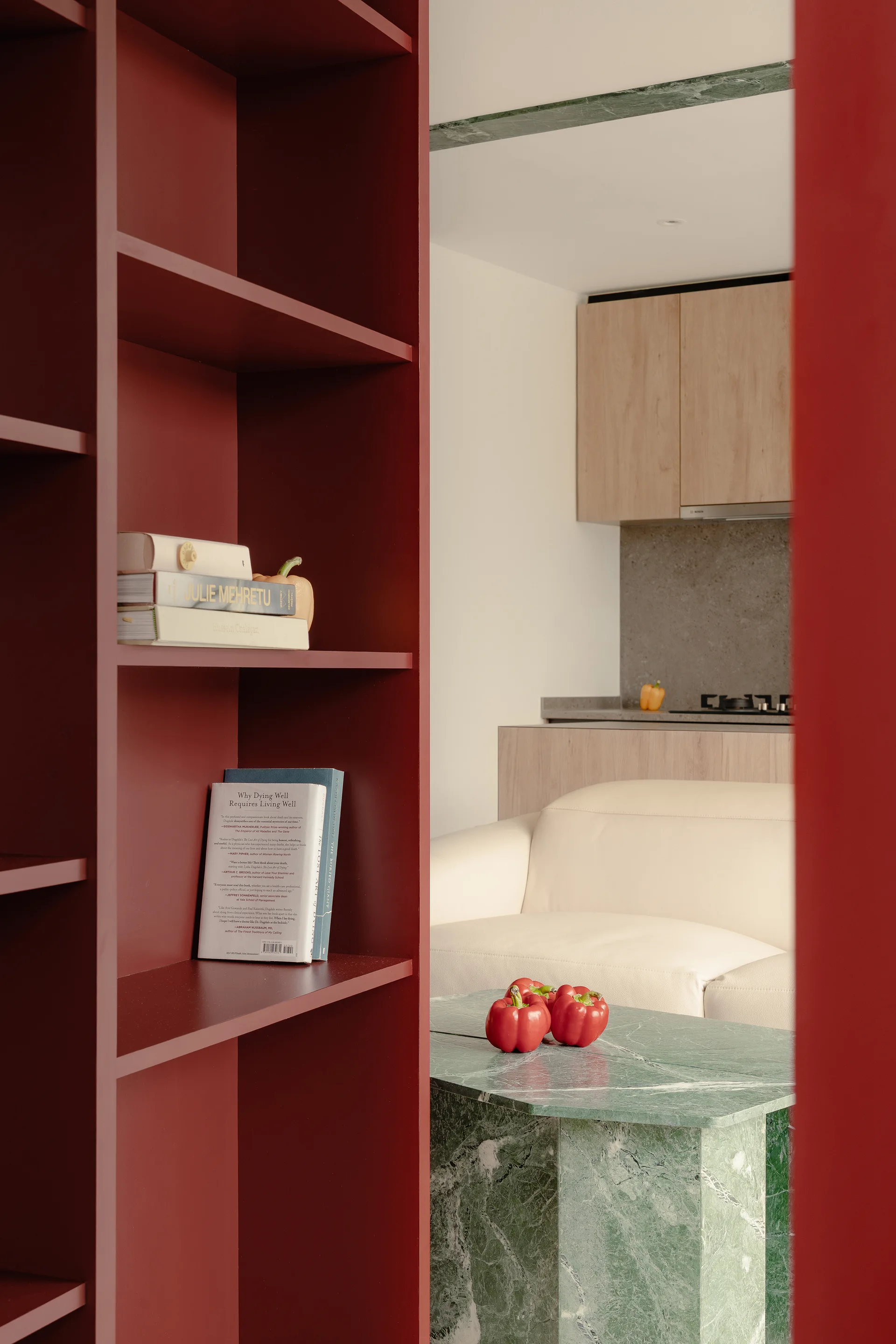 A matte red built-in shelving unit frames a contemporary living area featuring a green marble geometric coffee table and a cream sofa.