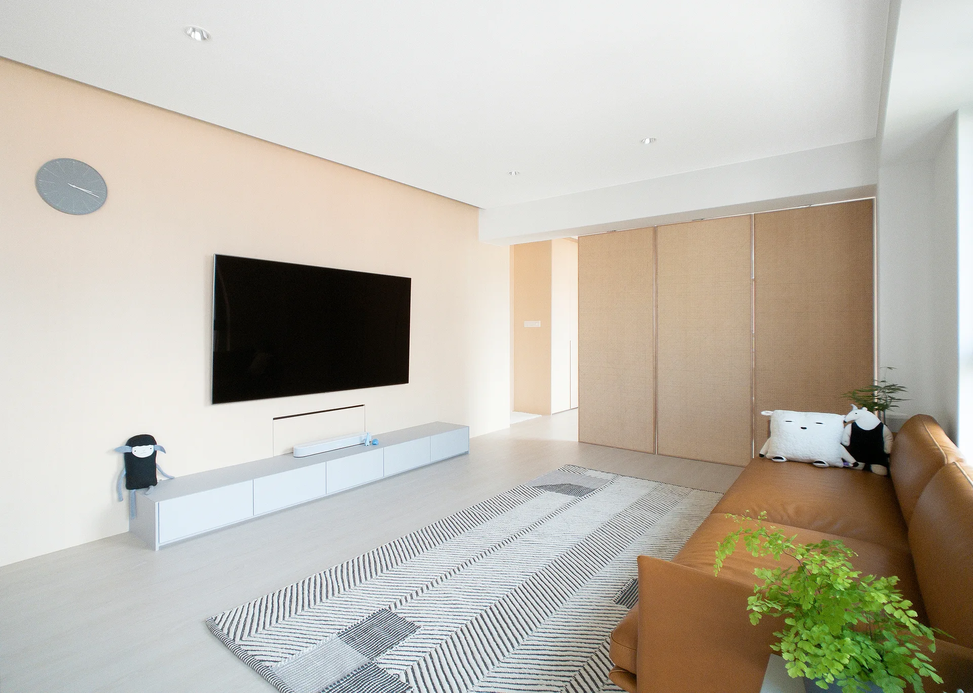 A minimalist living room features a tan leather sofa, a geometric patterned rug, a low-profile media console, and woven rattan sliding panels.
