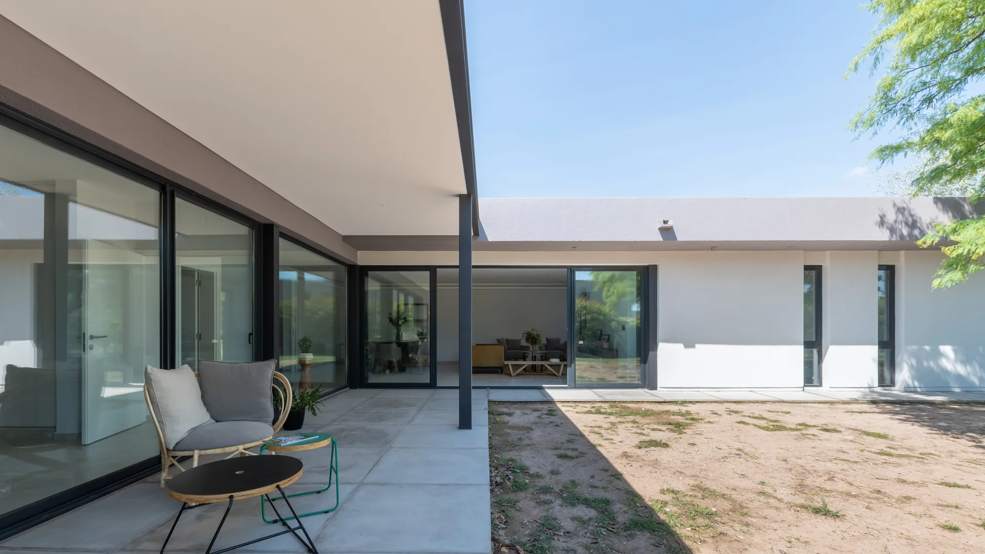 A modern covered patio features a concrete paver floor, a single rattan armchair with gray cushions, and sliding glass doors leading indoors.