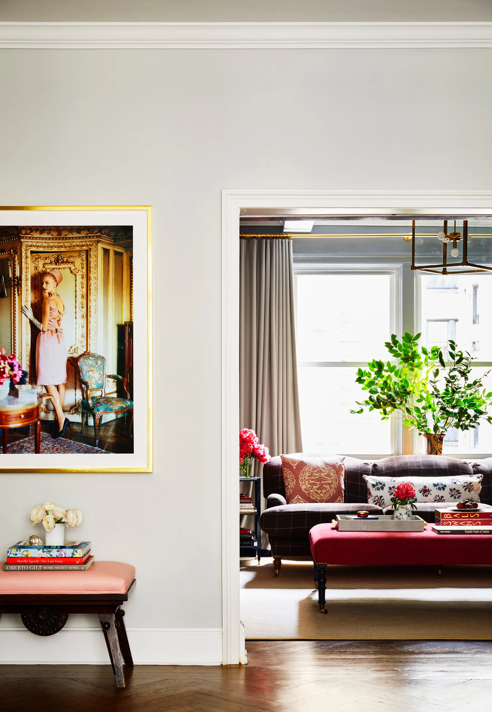 A view through a white doorway showing a living room with a plaid sofa, red ottoman, and a large framed photograph hanging on the foreground wall.