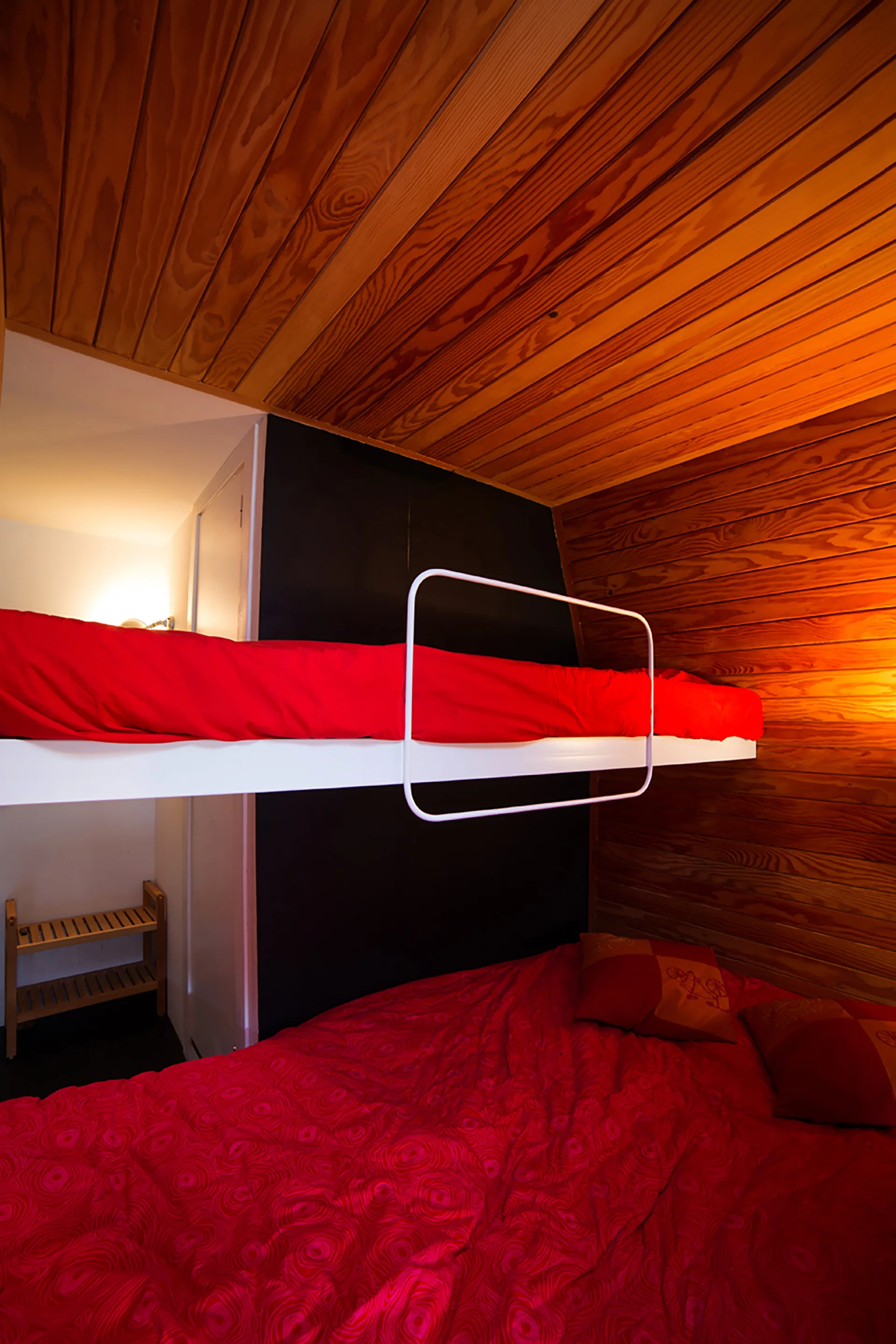 A cabin bedroom featuring built-in bunk beds with red bedding against horizontal wood paneled walls and a black accent wall.