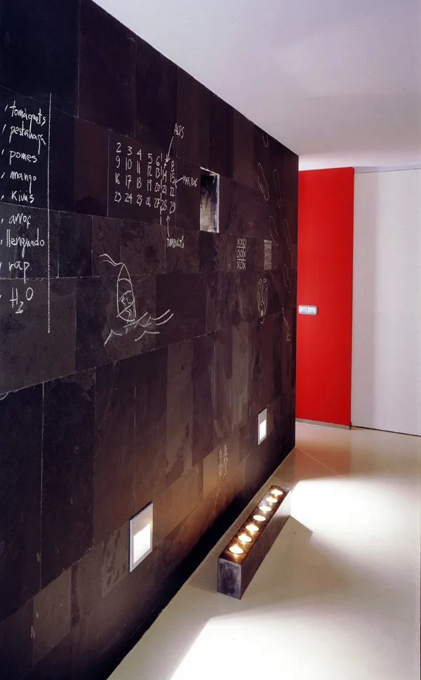 A modern hallway features a textured matte black tile accent wall decorated with white chalk drawings alongside integrated floor lighting.