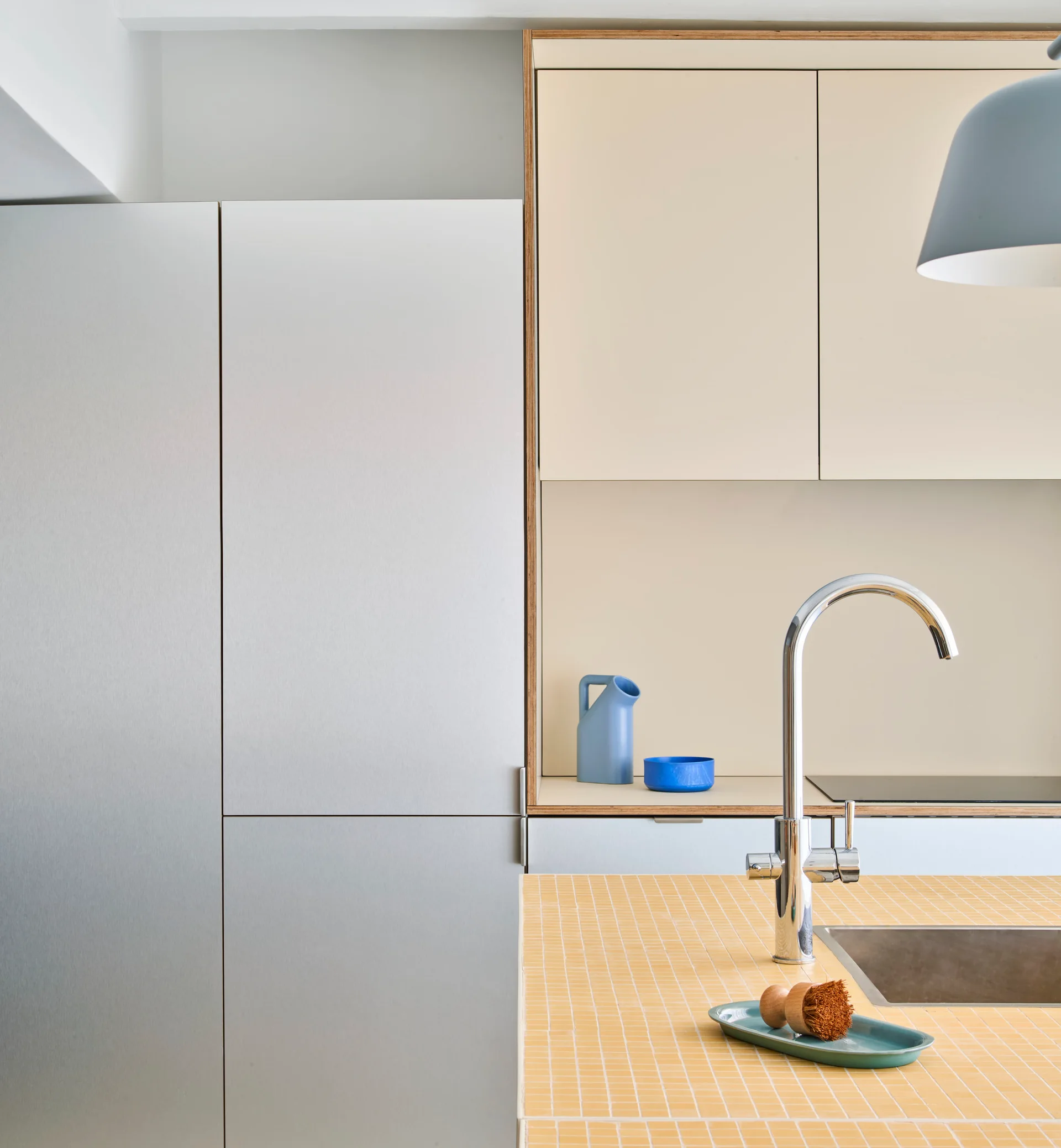 A modern kitchen island features a yellow tiled countertop with a chrome faucet next to beige cabinets.