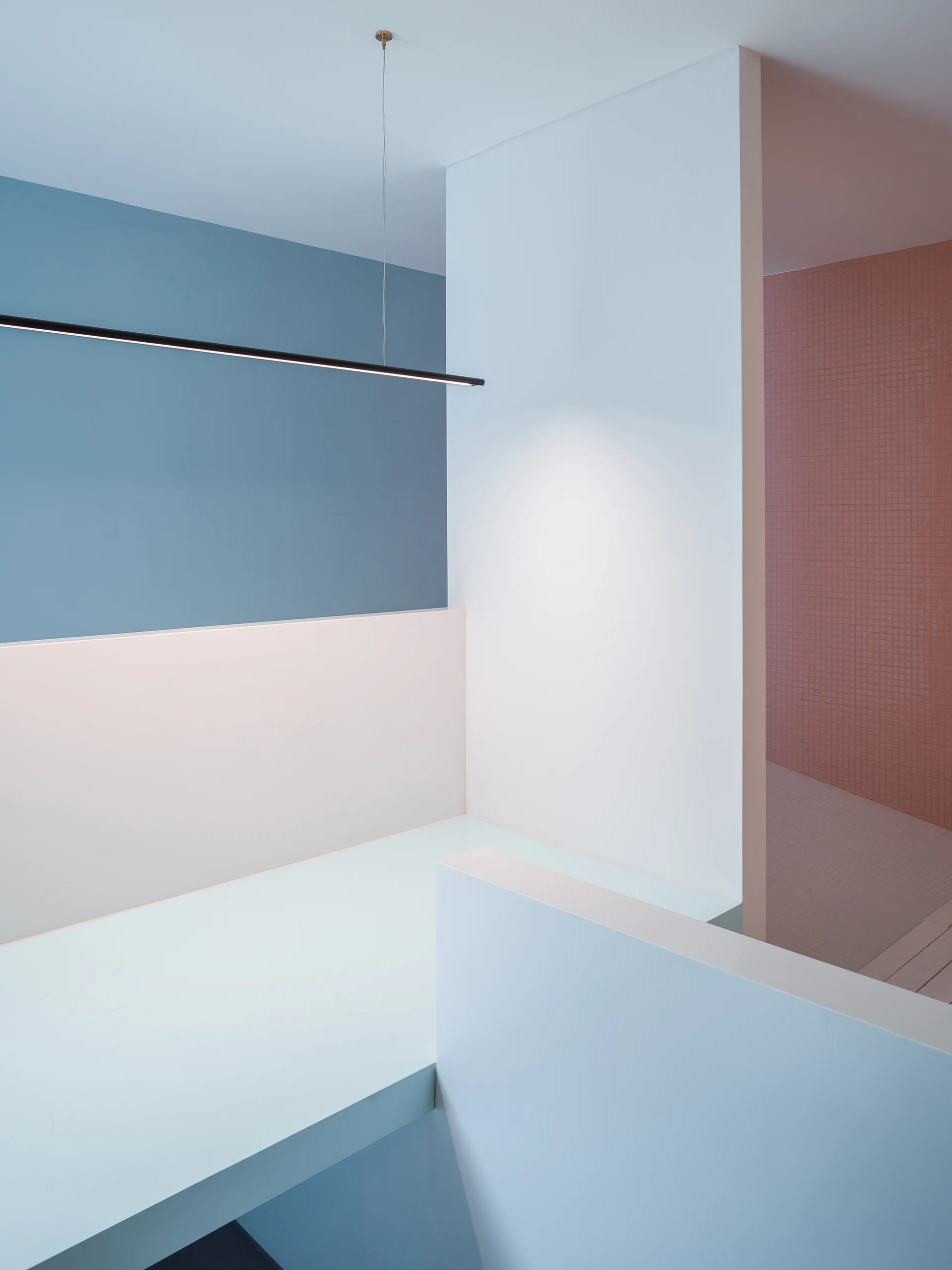 A minimalist staircase landing featuring white, blue, and light pink walls, a black linear pendant light, and a tiled pink background.