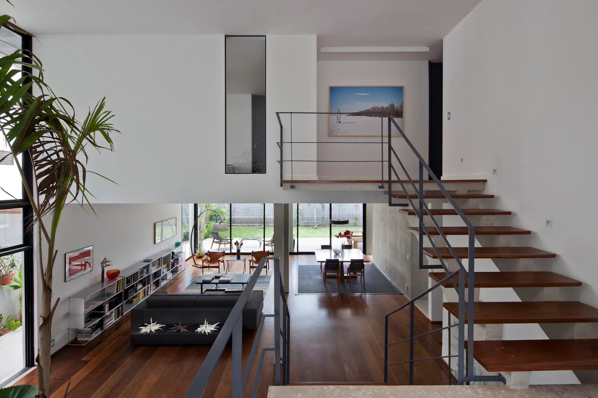 A high-angle view of an open-concept living space with dark wood floors, a modern dining area, and an open-riser wooden staircase with metal railings.