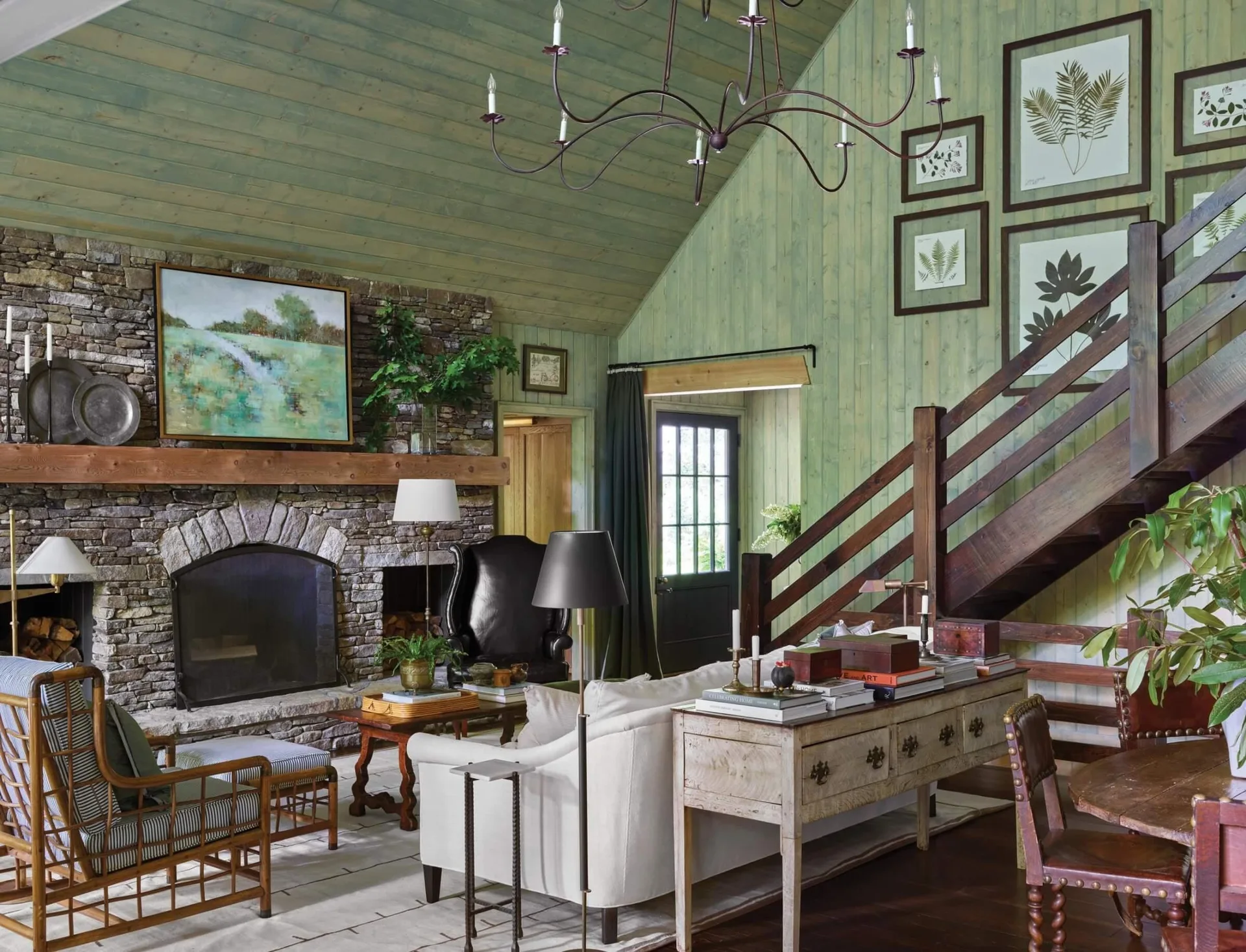 A rustic living room featuring sage green wood paneled walls, a vaulted ceiling, a stone fireplace, and a cream sofa with a console table.