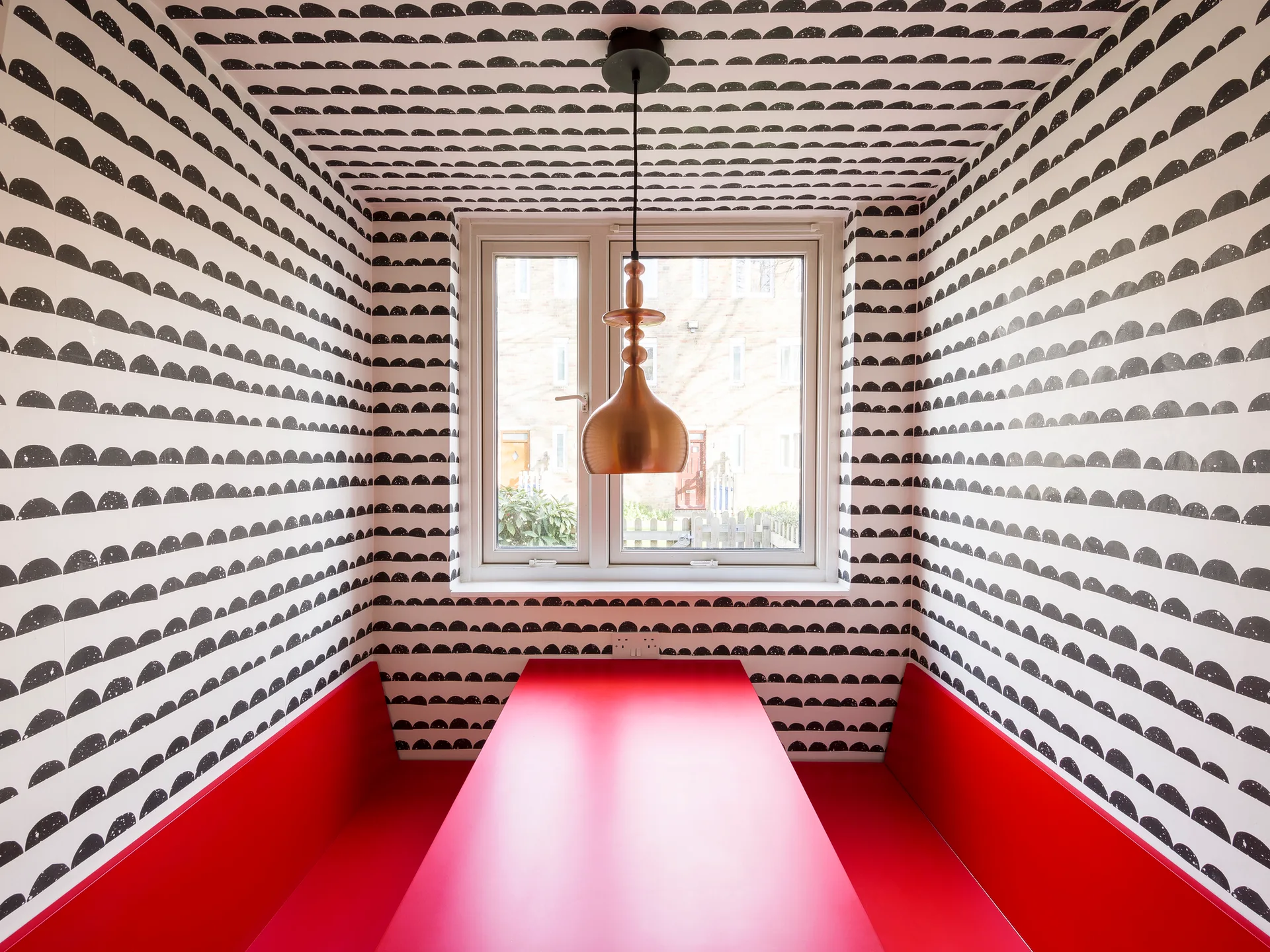 A small dining nook featuring a bright red table and built-in benches surrounded by black and white semi-circle patterned wallpaper.