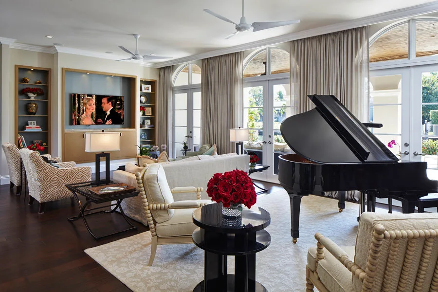A spacious living room featuring a black grand piano, a beige sofa, animal-print armchairs, and tall arched glass doors with drapes.