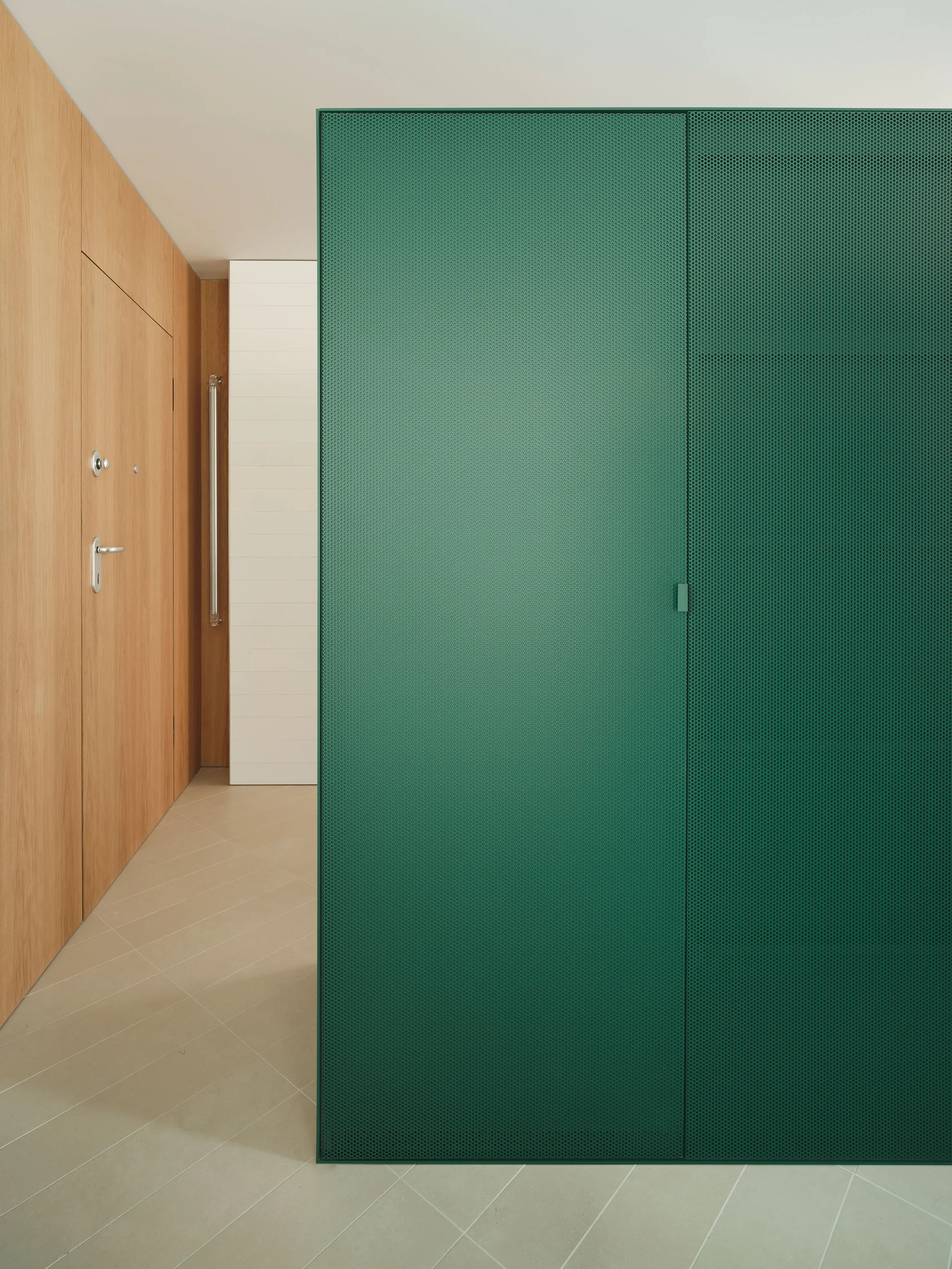 An entryway corridor features a green perforated metal screen next to light wood-paneled walls and a beige tiled floor.