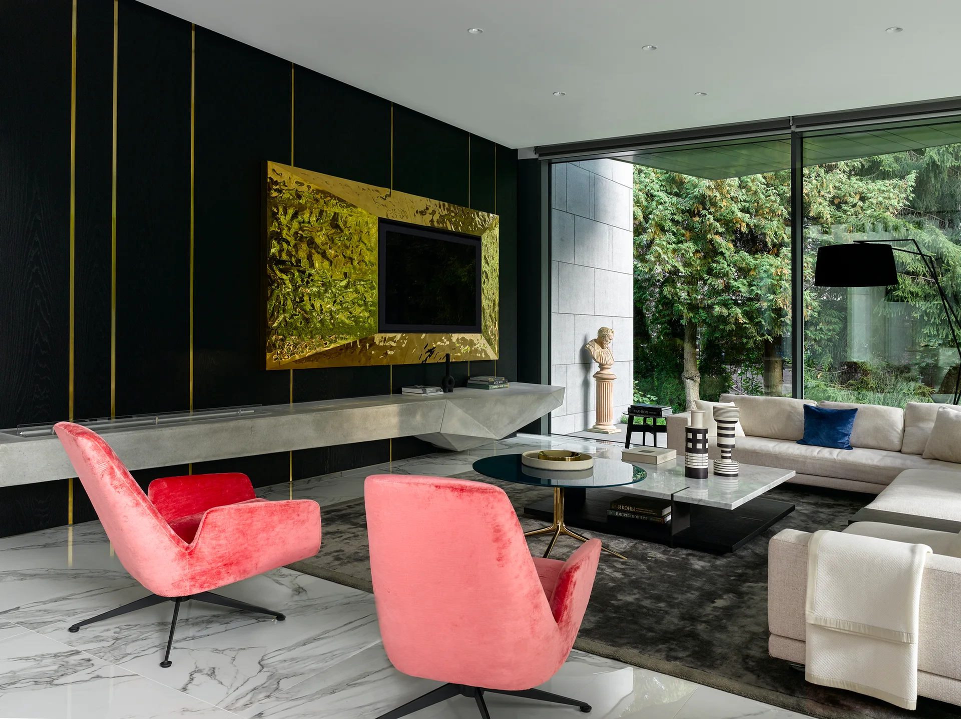 A modern living room features pink velvet armchairs and a cream sectional sofa on a marble floor in front of a black paneled wall.