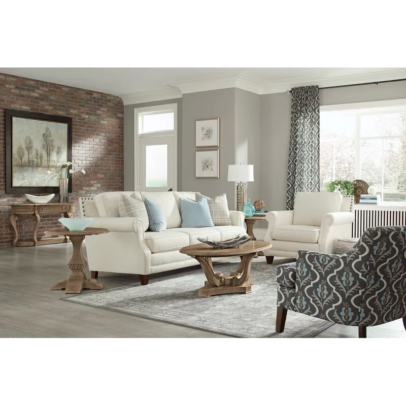 A traditional living room features a cream sofa, a blue patterned armchair, oval wooden tables, and a red brick accent wall.