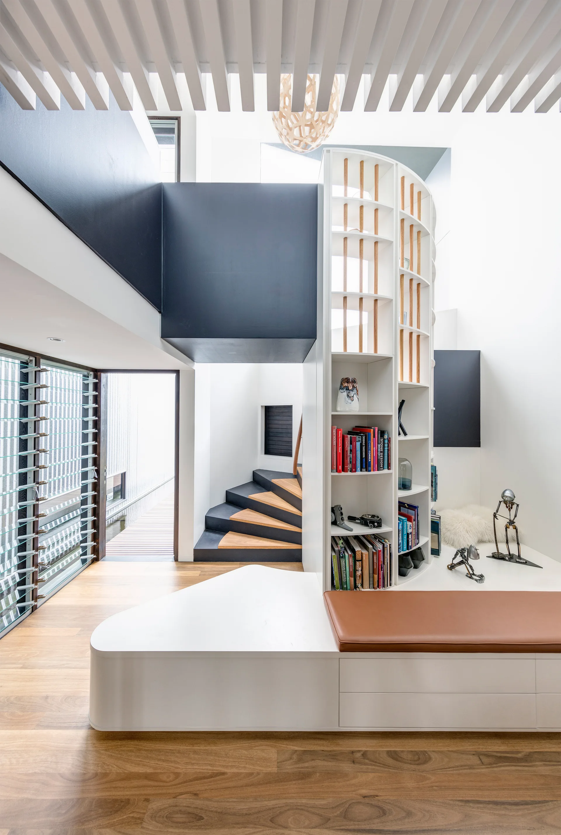 A contemporary staircase area with wood treads and black accents features a white curved bookshelf unit integrated with a low storage bench.