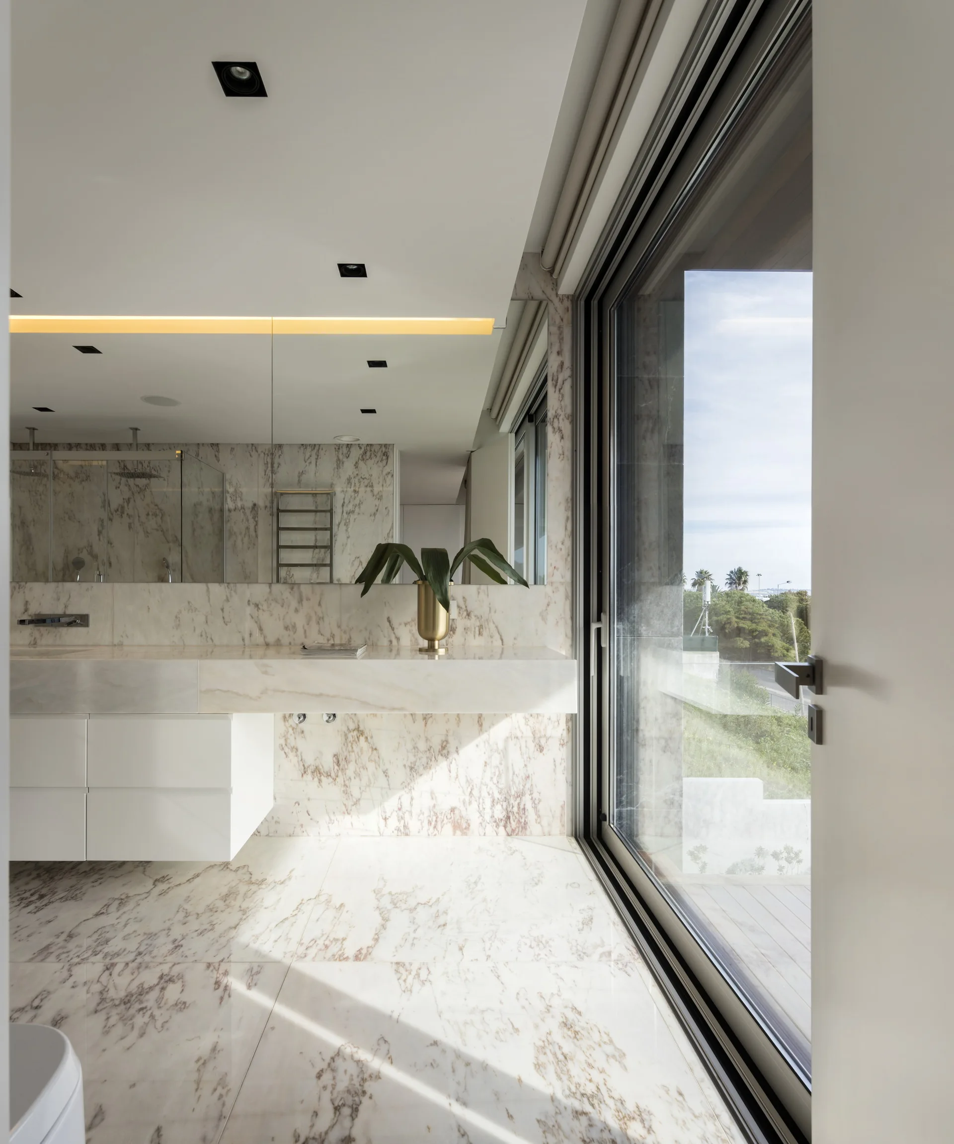 A modern bathroom features veined marble floors and walls, a floating white vanity with a large mirror, and a sliding glass door.
