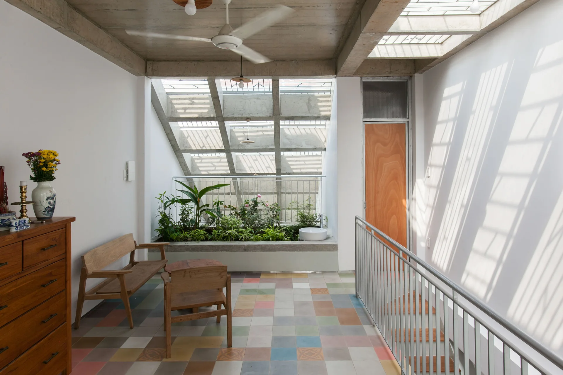 A bright landing area features a wooden bench, a colorful tiled floor, and a built-in planter filled with greenery beneath an angled skylight.