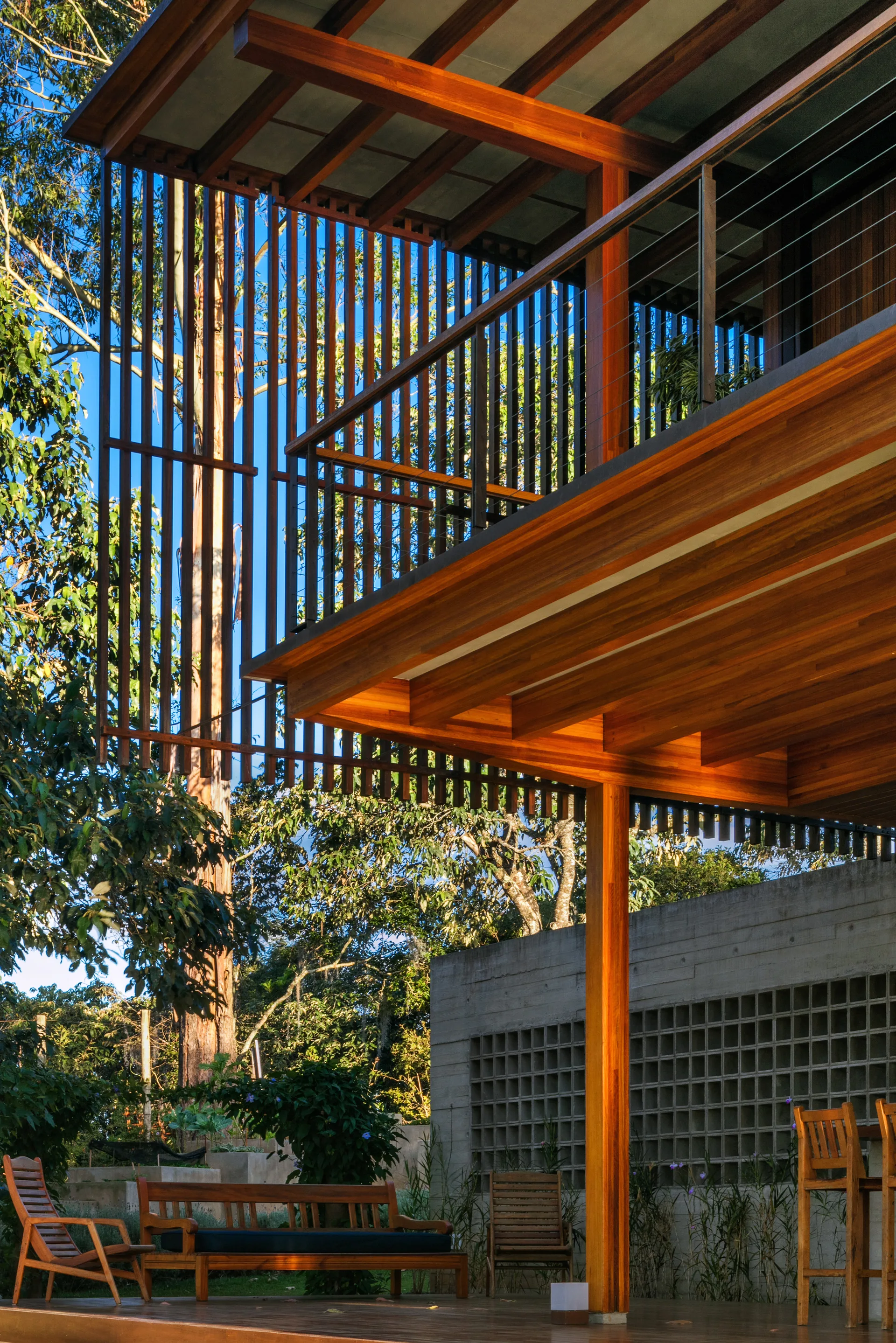 A covered wood patio features a double-decker timber roof structure, a slatted privacy screen, wooden outdoor furniture, and a concrete breeze-block wall.
