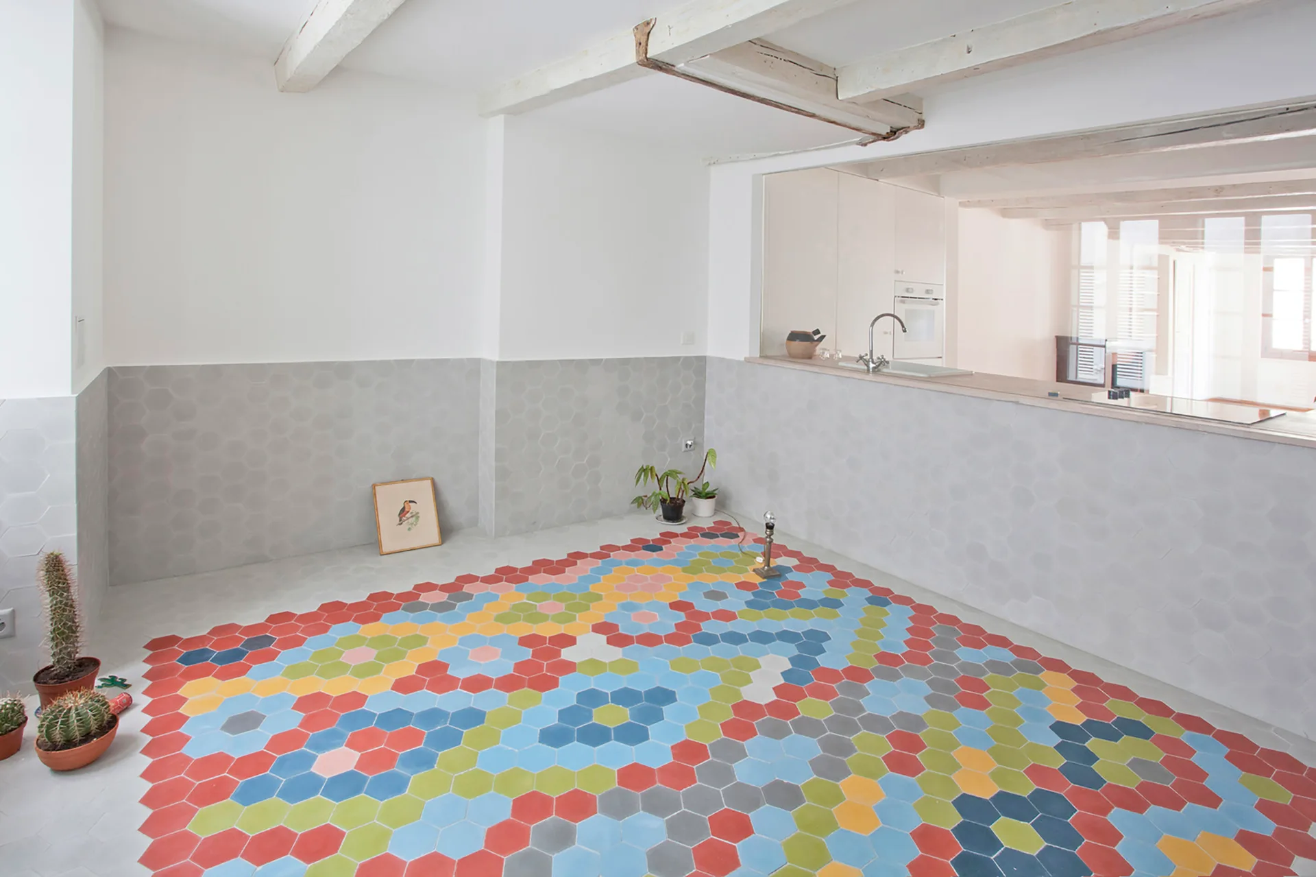 A bright room featuring a colorful hexagonal tile floor, light grey hexagonal wall tiles, and exposed rustic wood ceiling beams.