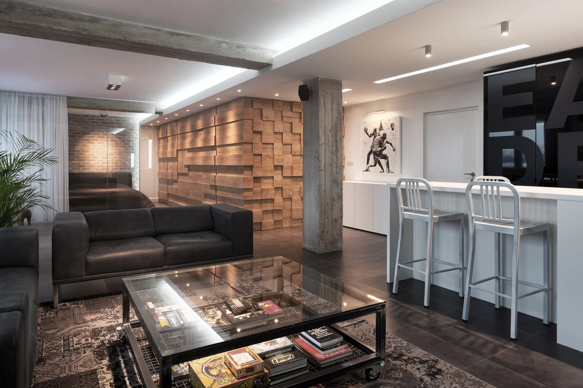 A modern industrial loft living room with a black leather sofa, glass coffee table, exposed concrete column, and a textured wood block wall.