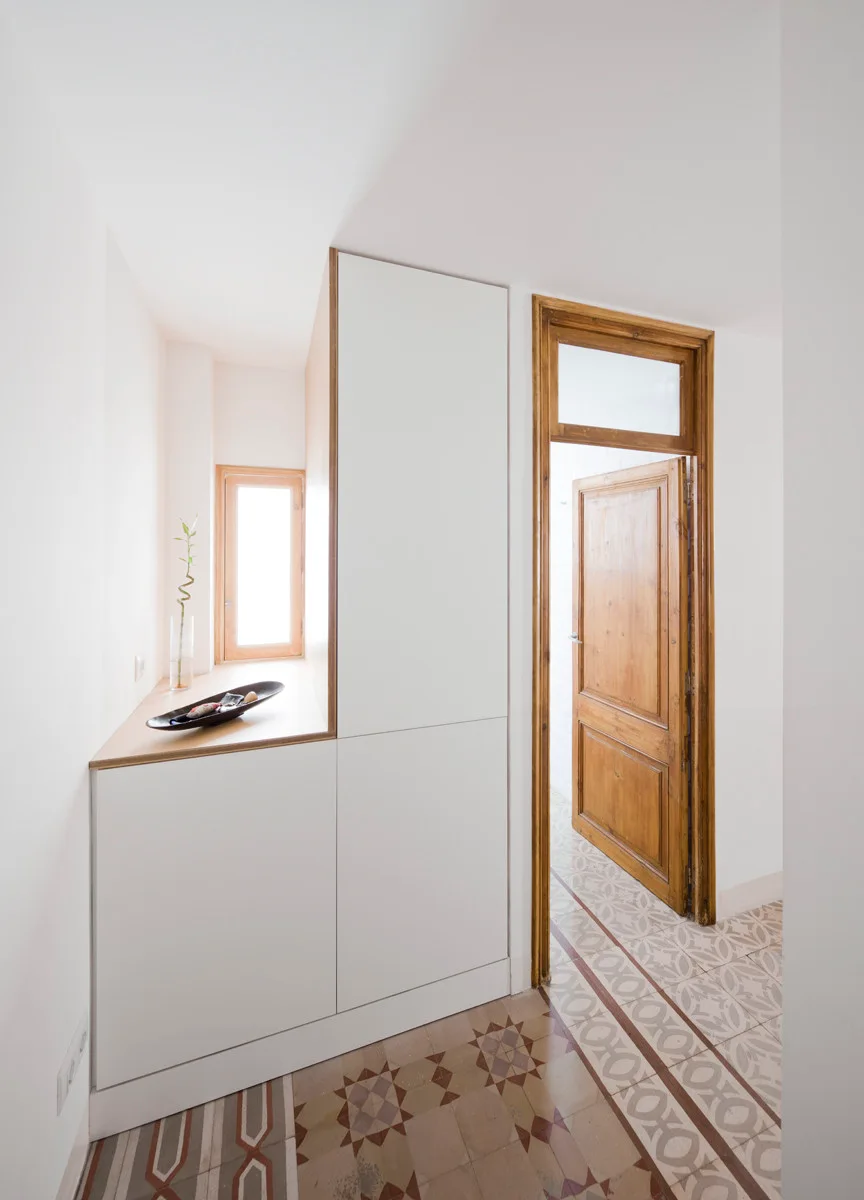 A bright hallway features custom white built-in storage cabinets alongside a natural wood door and geometric patterned floor tiles.