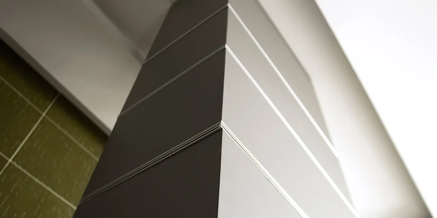 A close-up view of a grey architectural column wrapped in matte panels separated by thin horizontal metal trim reveals.