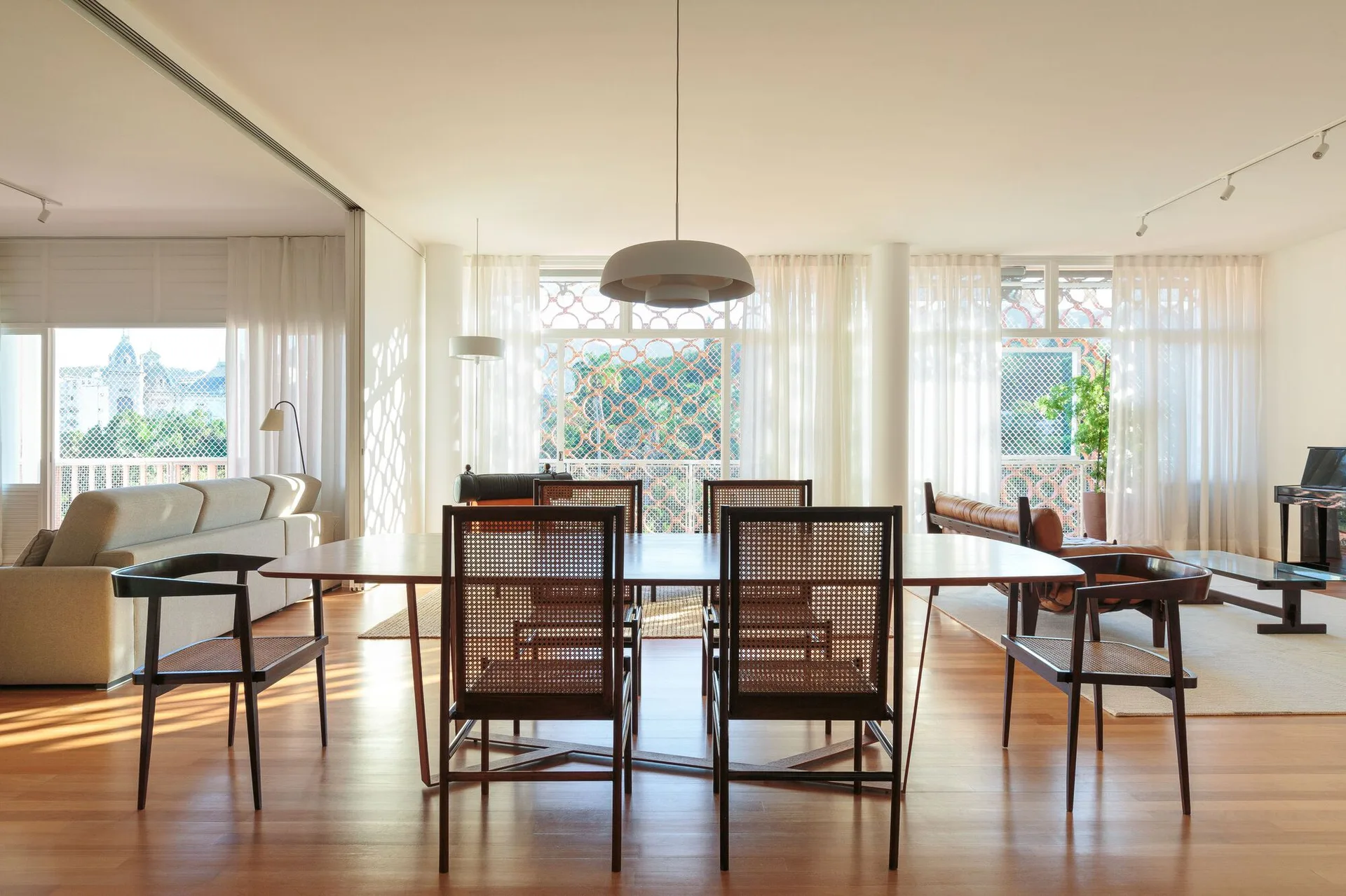 A spacious dining room features a long wooden dining table surrounded by cane-back chairs under a large grey pendant light.