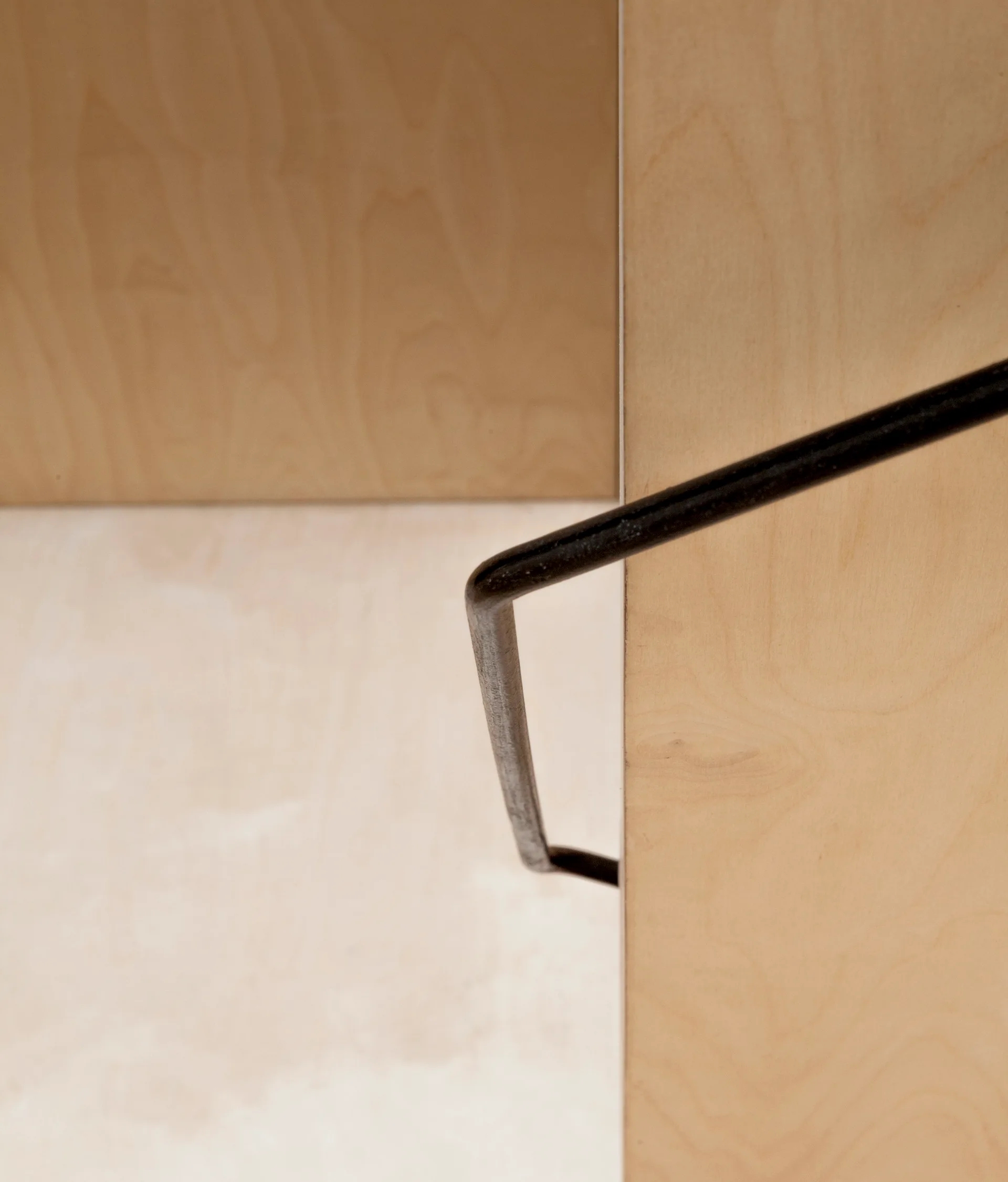A close-up of a minimalist staircase featuring a slender black metal handrail mounted to light plywood walls.