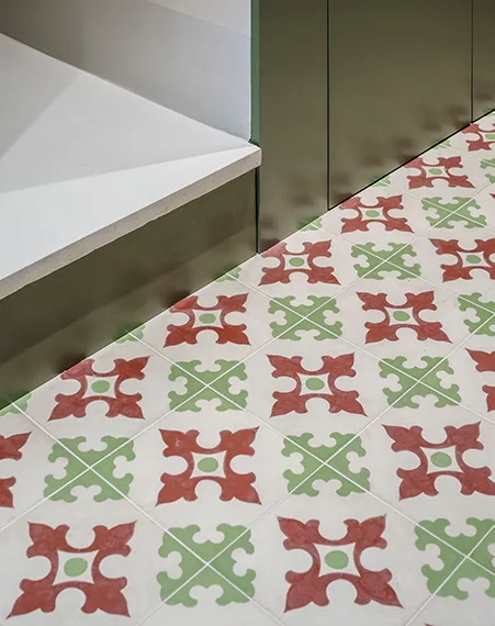 A close-up view of a matte tile floor with a red and green geometric pattern meeting a solid olive green metal baseboard.