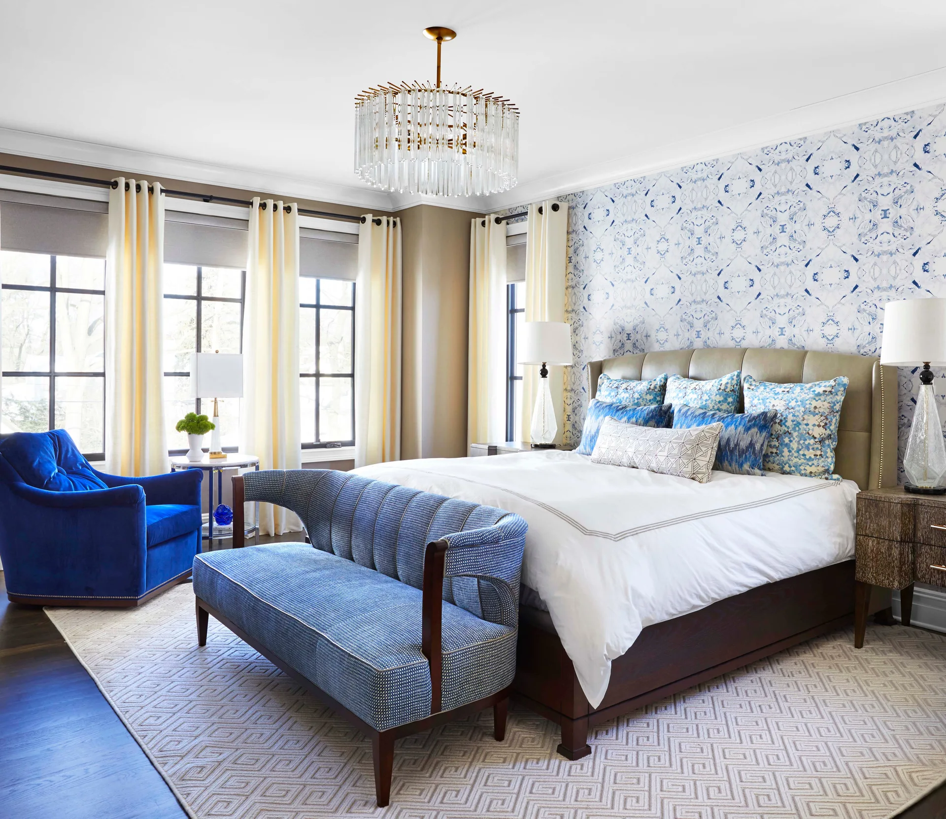 Transitional bedroom with a blue patterned wallpaper accent wall, a bed with coordinating pillows, and a blue settee on a geometric rug.