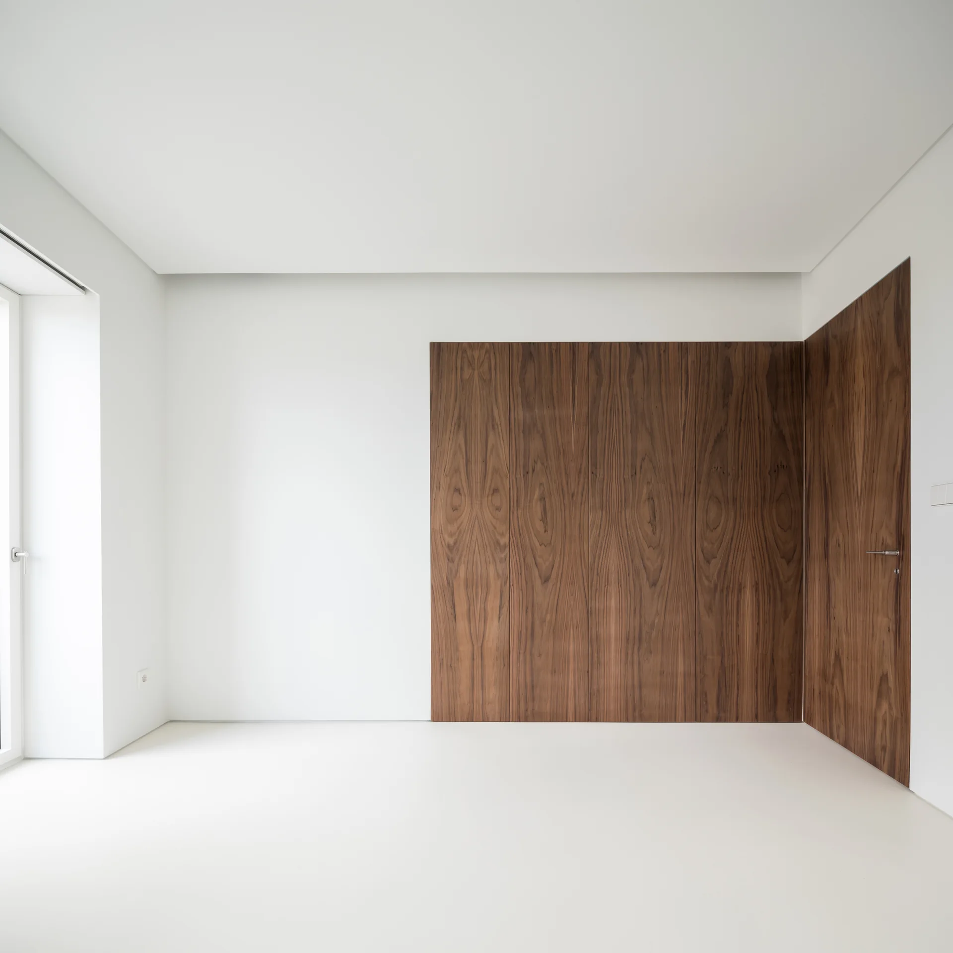 An empty minimalist white room featuring a corner clad in rich brown wood veneer panels with a matching integrated flush door.