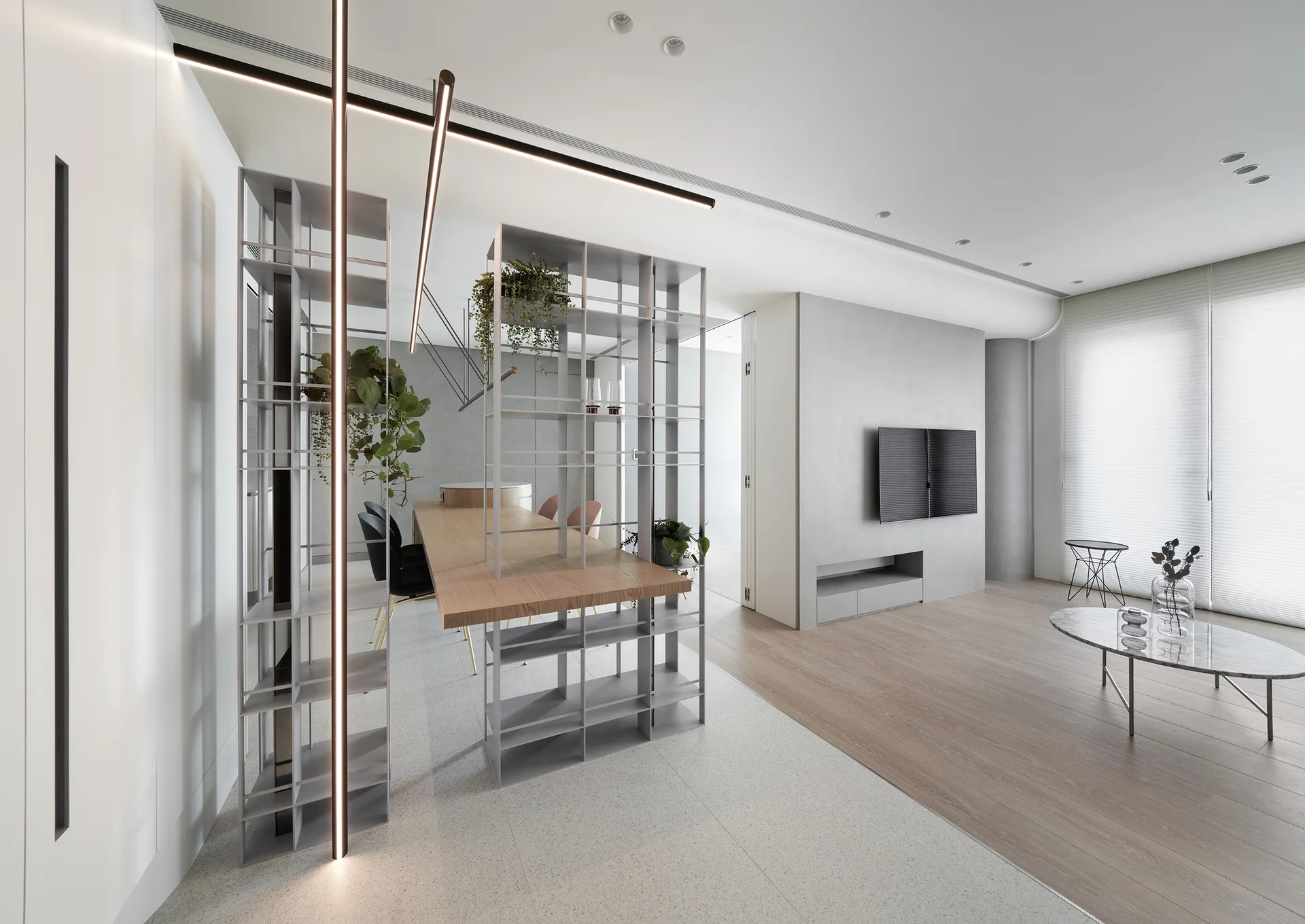 A modern open-plan living and dining space with a metal shelving room divider integrated with a wooden table on a tile and wood floor.