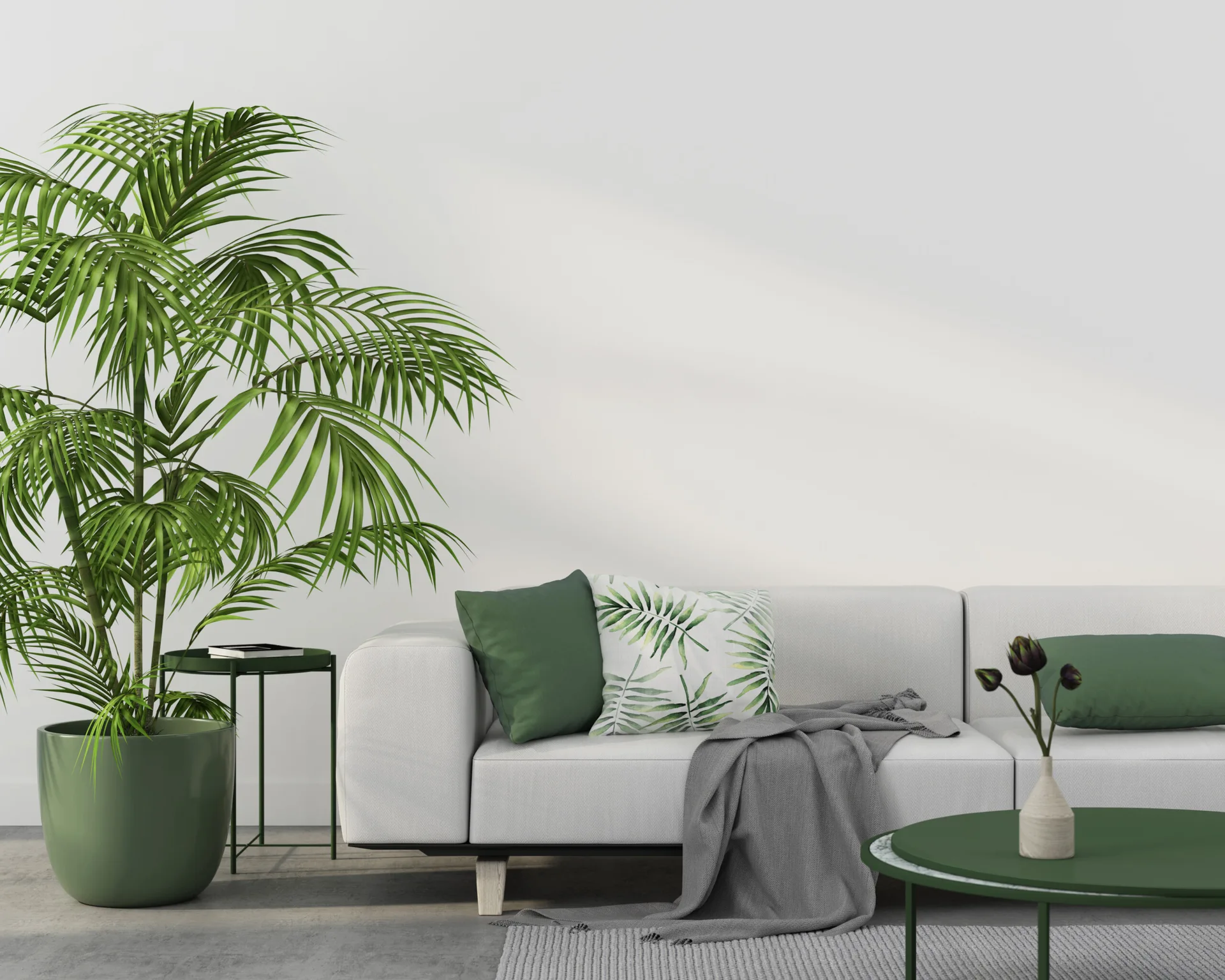 A white sectional sofa features green and botanical print pillows alongside a large potted palm, green coffee tables, and a grey rug.