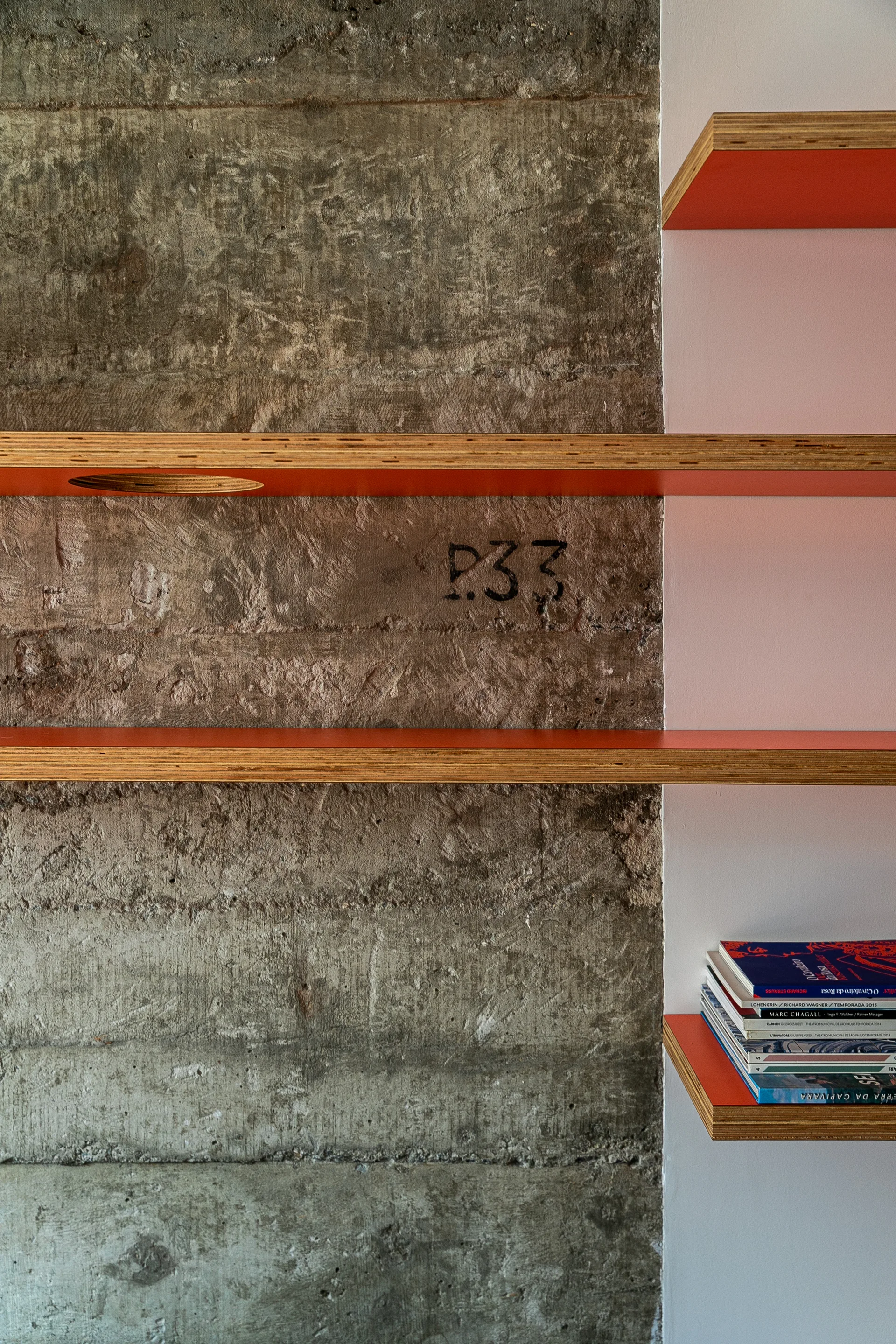 A close-up of custom orange laminate plywood shelves mounted on a rough grey concrete wall and a smooth white wall.