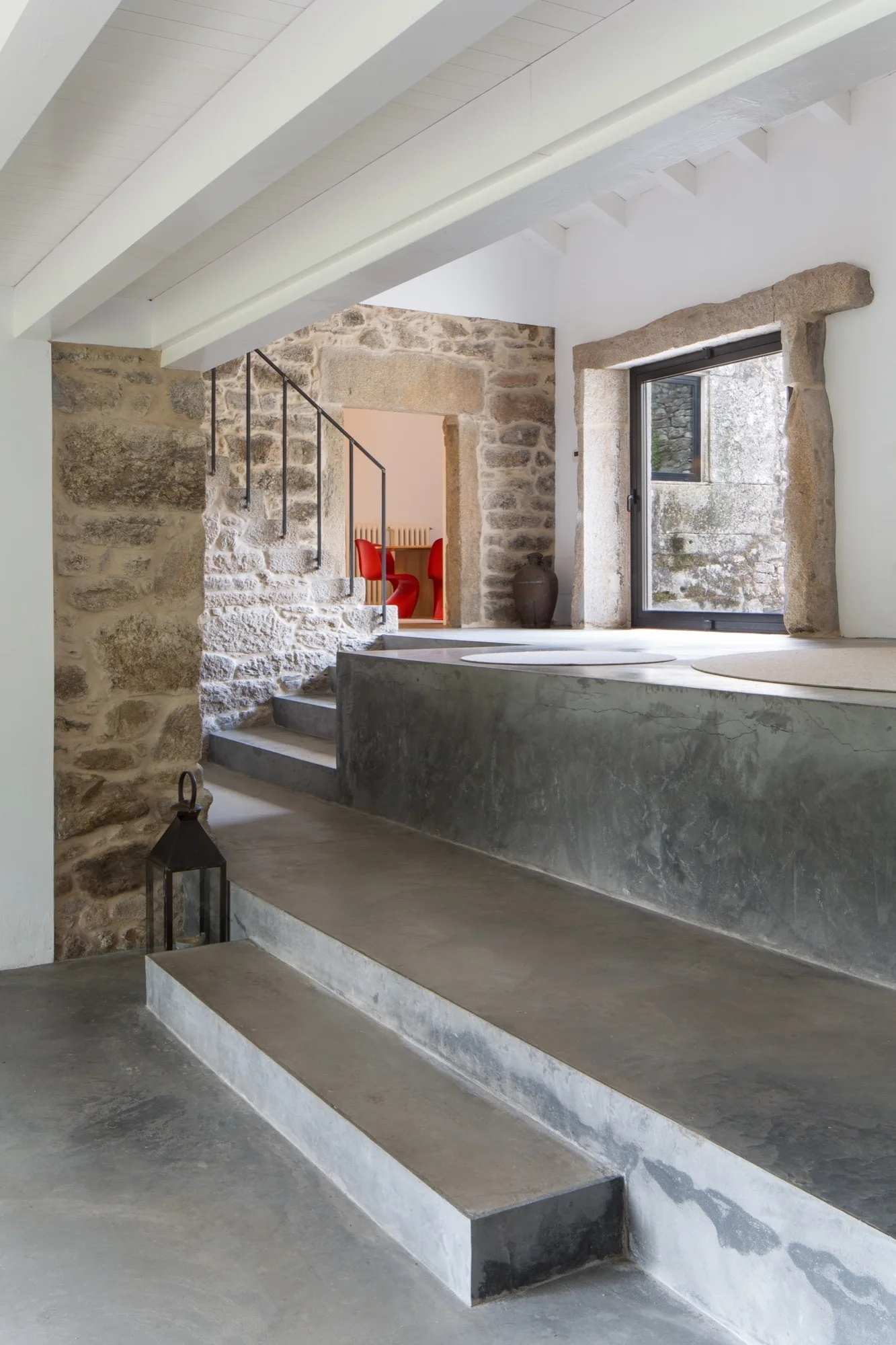 Cast concrete steps and a raised platform lead up to an entryway featuring rough exposed stone walls and white painted wood ceiling beams.