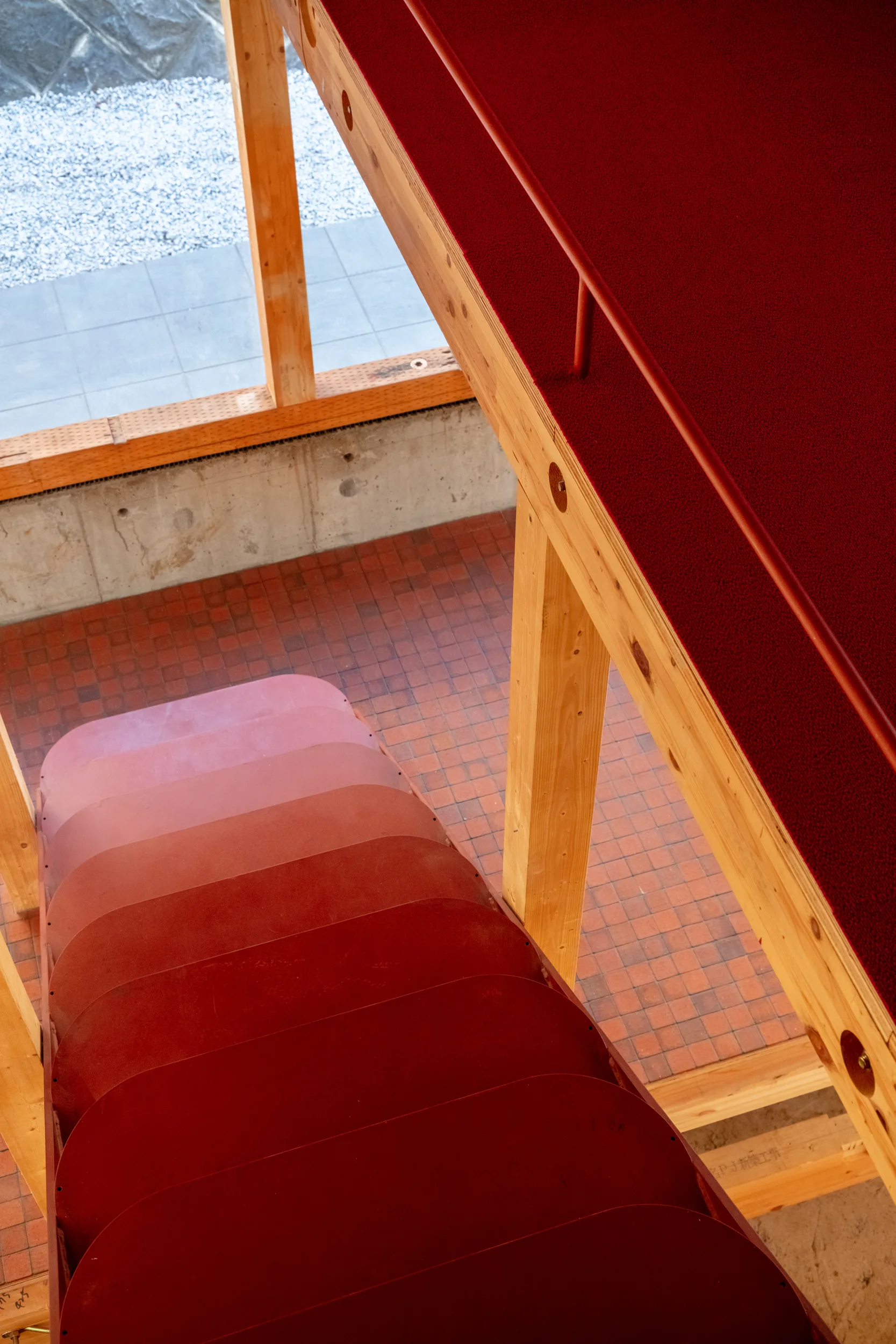 High-angle view of a saturated red metal staircase with curved steps surrounded by light wood structural columns and a red tile floor.