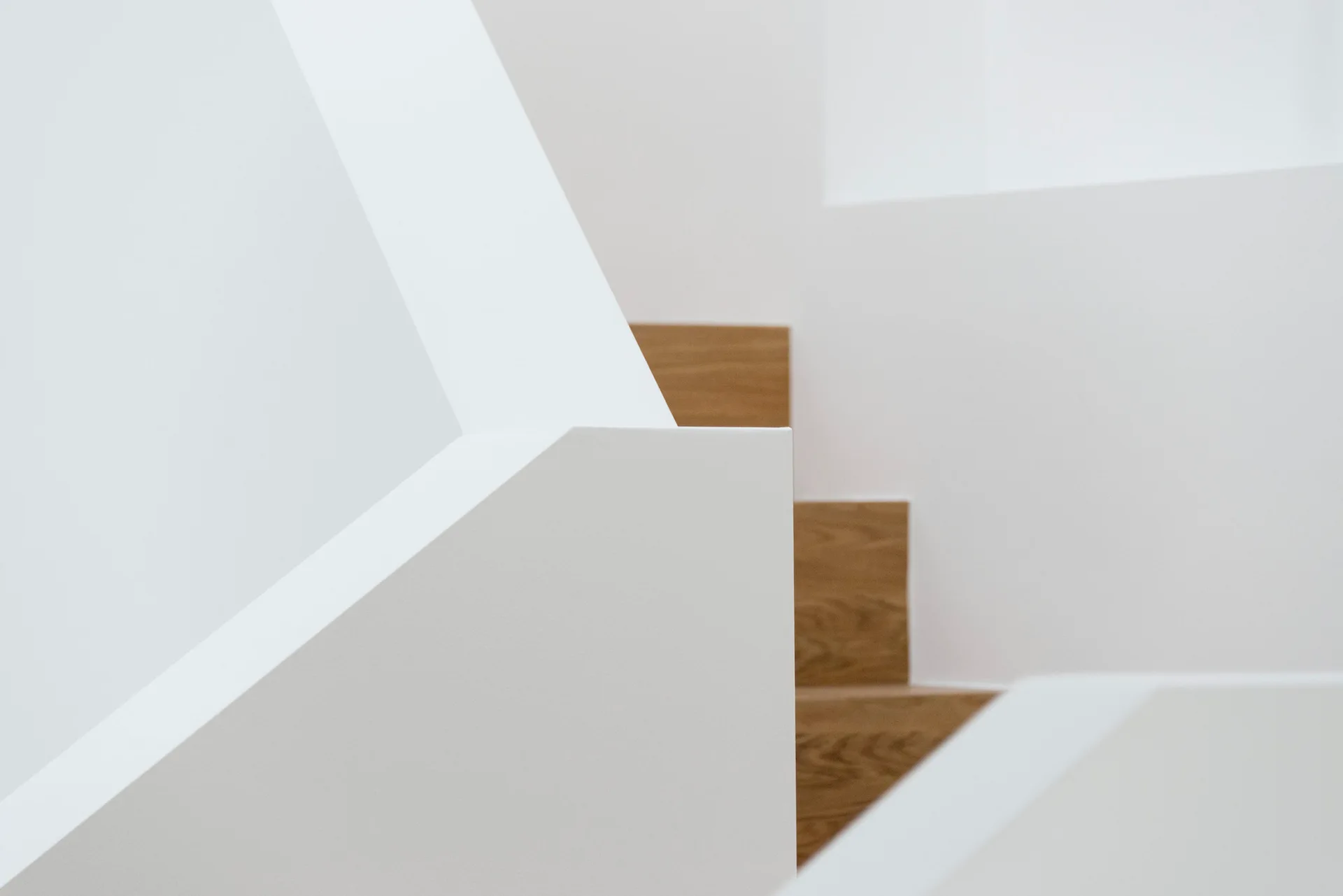 A close-up view of a minimalist white geometric staircase with warm wood treads and smooth painted walls.